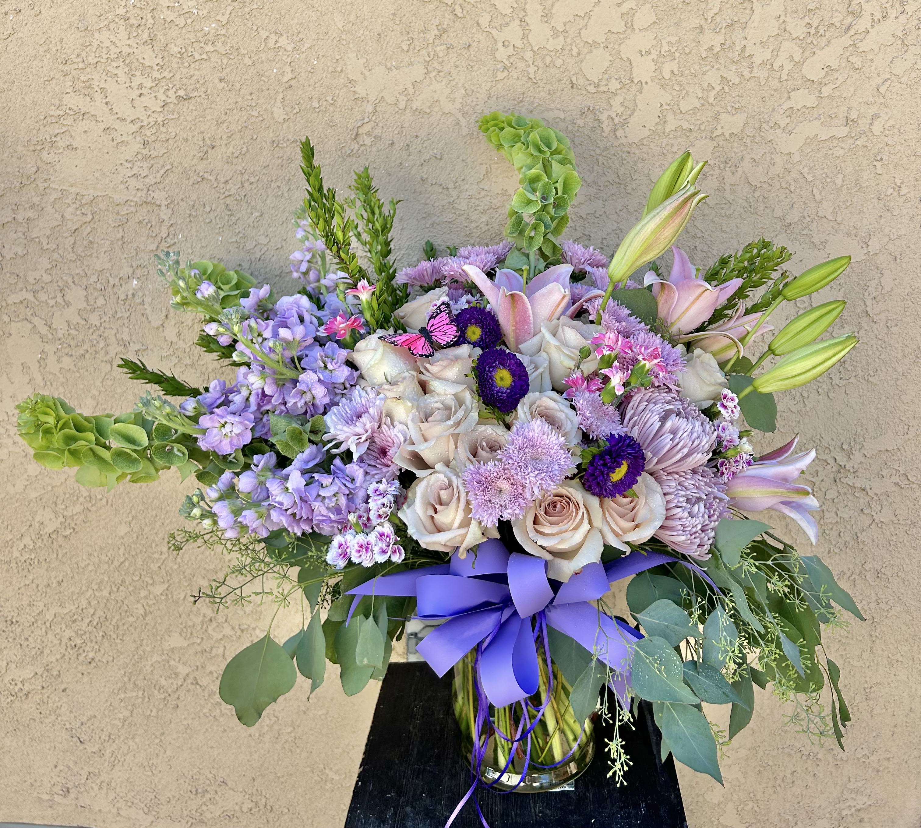Sweet Sights - Beautiful arrangement of lavender and purple stock, roses, lilies, bells of ireland, delphinium and green accents