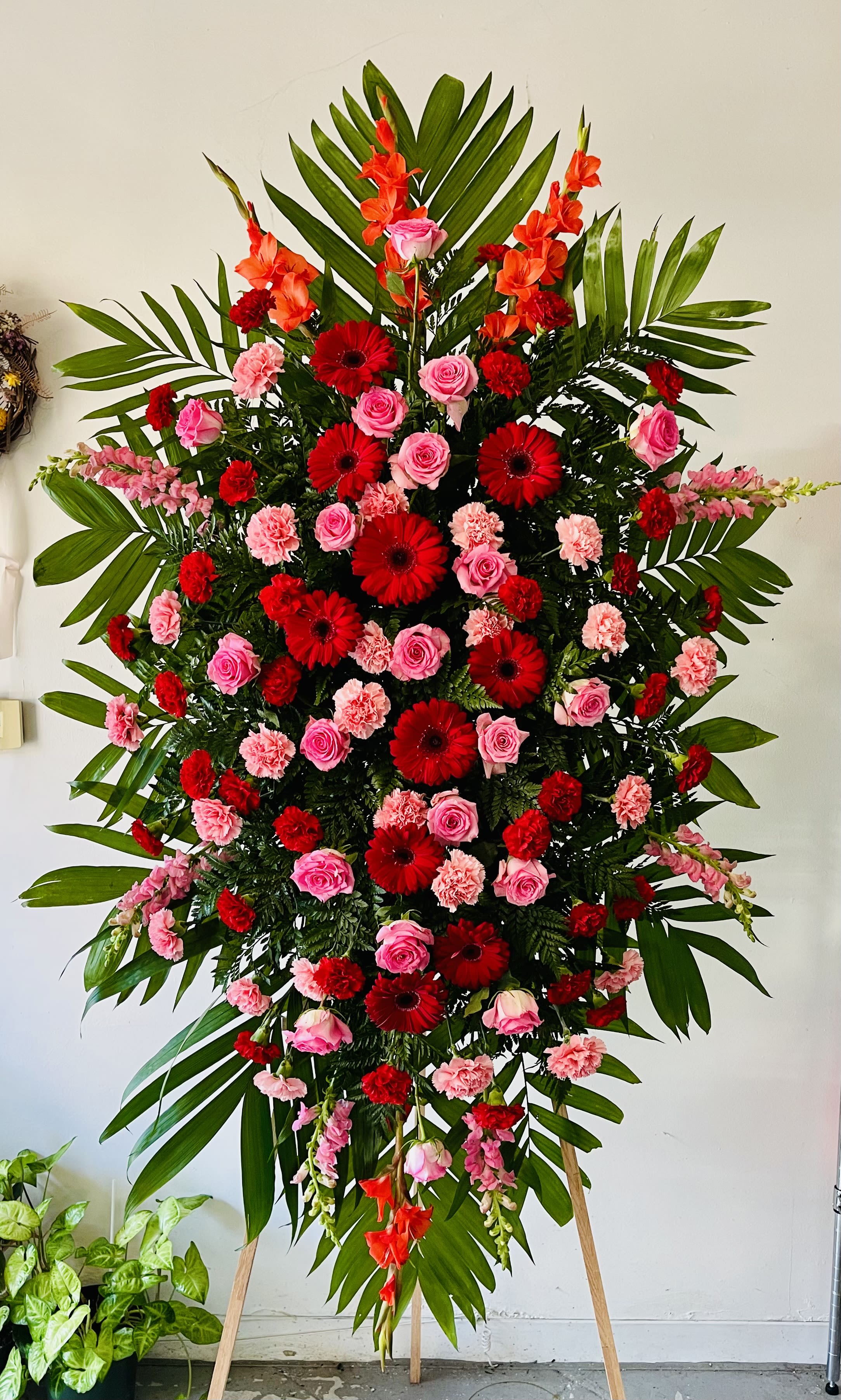 Elegant Tribute - Pink & Red Elegant Tribute - Pink & Red - The Elegant Tribute - Pink & Red Spray is a vibrant display of love and affection. Pink and Red roses, carnations, gerbera daisies and more are artfully arranged amongst emerald palm fronds and lush greens. This standing spray is an excellent way to honor the life of your loved one. Optional Banner included upon request. Include your banner message in the Florist Instructions during checkout, or give us a call at (562)692-0438.