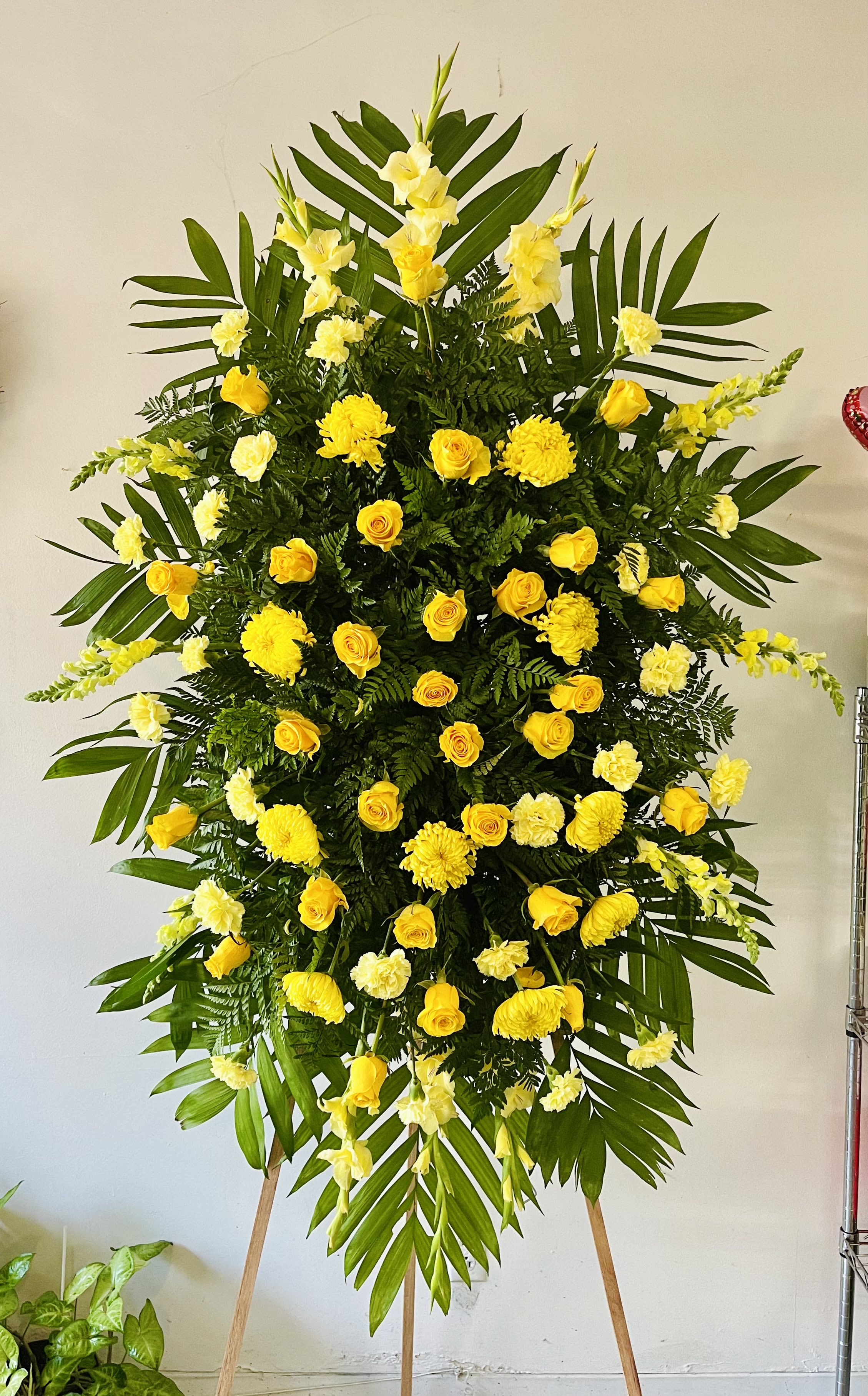Elegant Tribute - Yellow Elegant Tribute - Yellow - The Elegant Tribute - Yellow Spray is an exquisite display of sweet serenity. Yellow roses, crysanthemums, carnations and more are artfully arranged amongst emerald palm fronds and lush greens. This standing spray is an excellent way to honor the life of your loved one. Optional Banner included upon request. Include your banner message in the Florist Instructions during checkout, or give us a call at (562)692-0438.