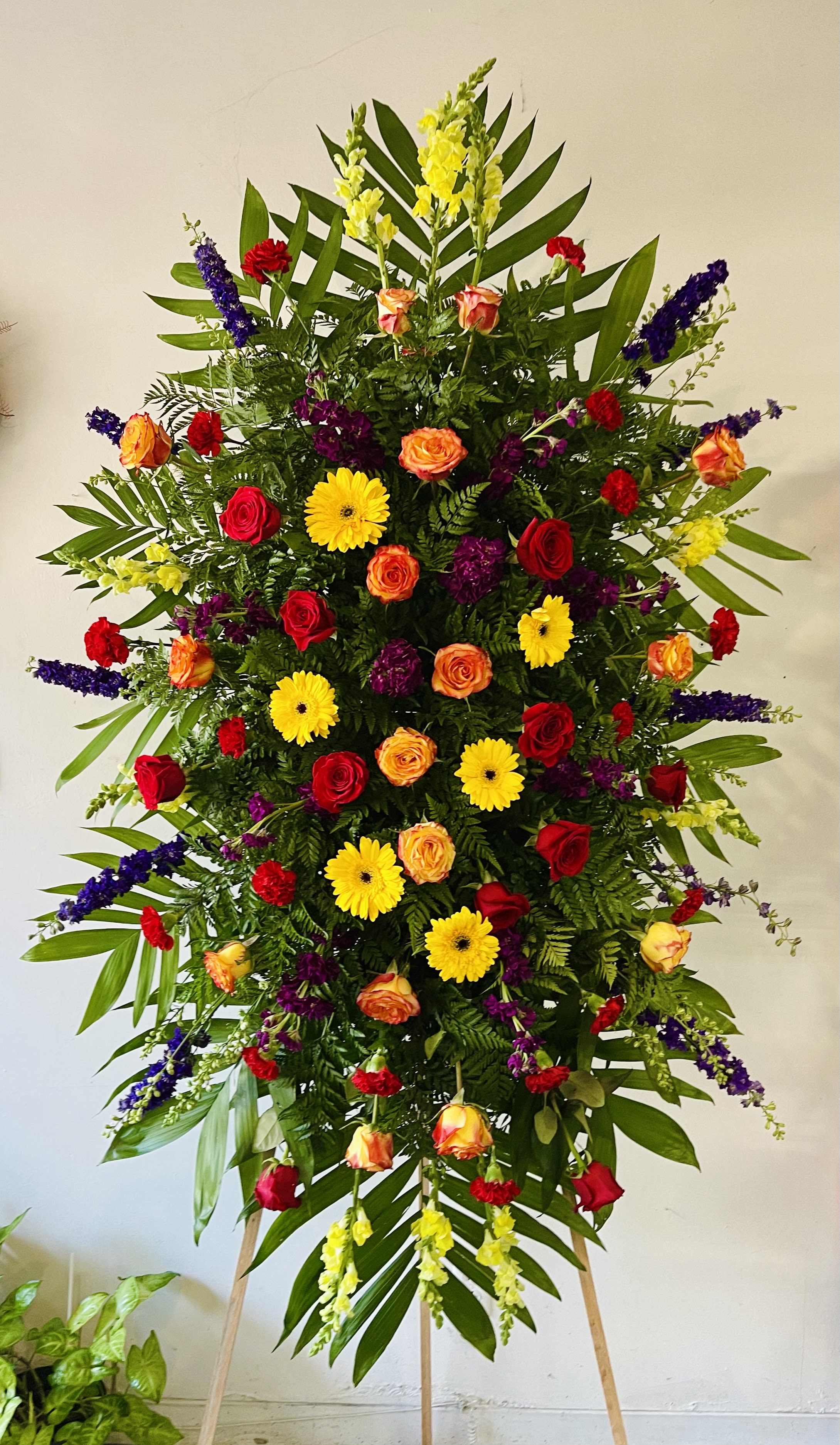 Elegant Tribute - Vibrant Elegant Tribute - Vibrant - The Elegant Tribute - Vibrant is a stunning display of love and affection. A beautiful array of colors featuring red and orange roses, yellow gerbera daisies and snaps, purple stock and larkspur and more are artfully arranged amongst emerald palm fronds and lush greens. This standing spray is an excellent way to honor the life of your loved one. Optional Banner included upon request. Include your banner message in the Florist Instructions during checkout, or give us a call at (562)692-0438.
