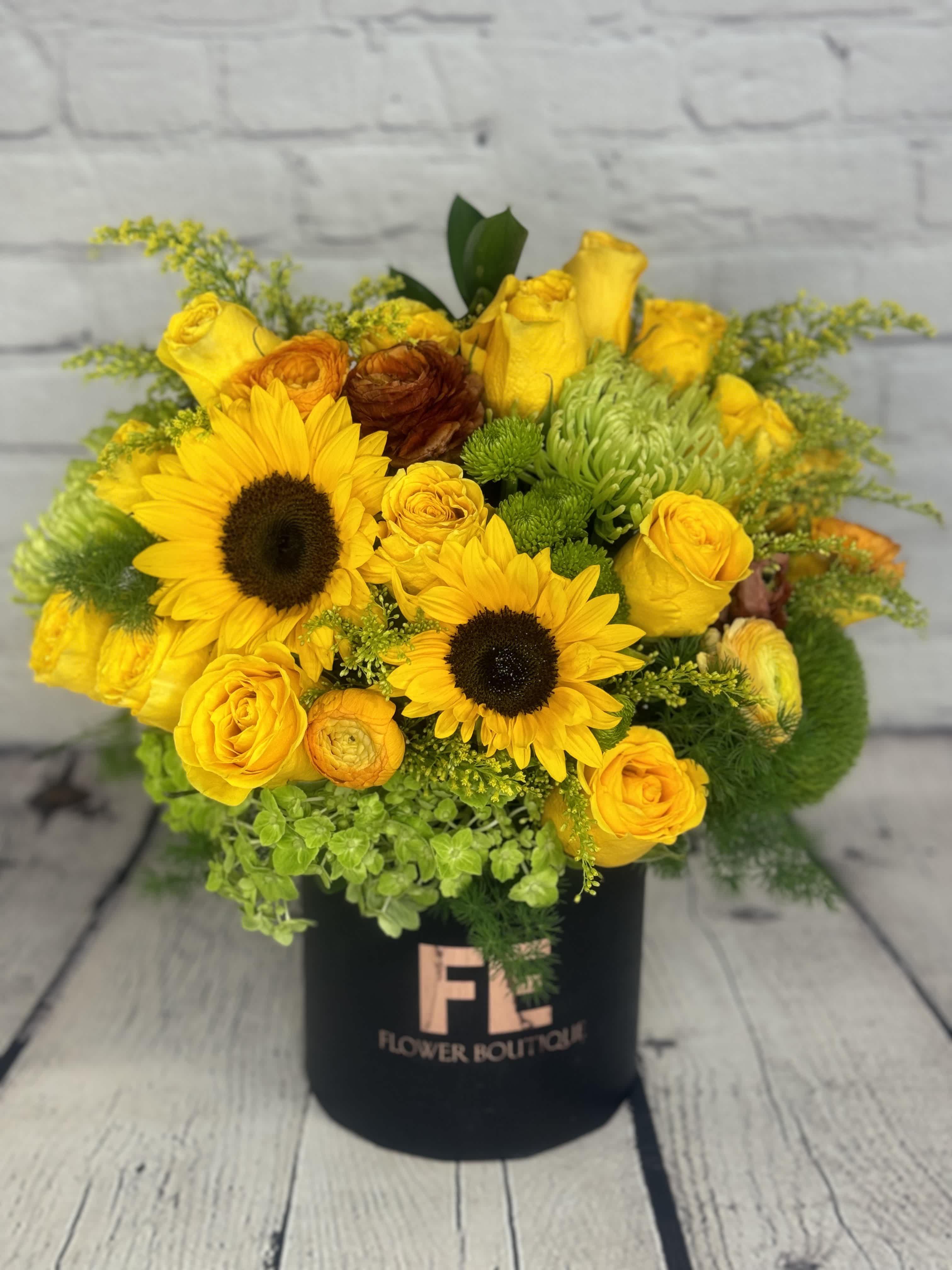 Yellow Mellow  - Yellow Mellow is a charming and exquisitely designed flower arrangement that highlights the beauty of yellow flowers. This floral arrangement features a stunning combination of yellow roses (15), sunflowers, ranunculus, dianthus, mums, green buttons, solidago, and lush green hydrangea.   This beautiful arrangement is presented in a sleek black box, adding an elegant touch to its natural beauty. The brilliant yellow tones of the flowers stand out beautifully against the deep black box, creating an incredibly appealing sense of contrast.  Yellow Mellow is perfect for conveying appreciation, adoration, and gratitude to a loved one or friend. It is also an excellent choice for the holiday seasons and other special occasions such as birthdays, and anniversaries, or just to express a loving sentiment.