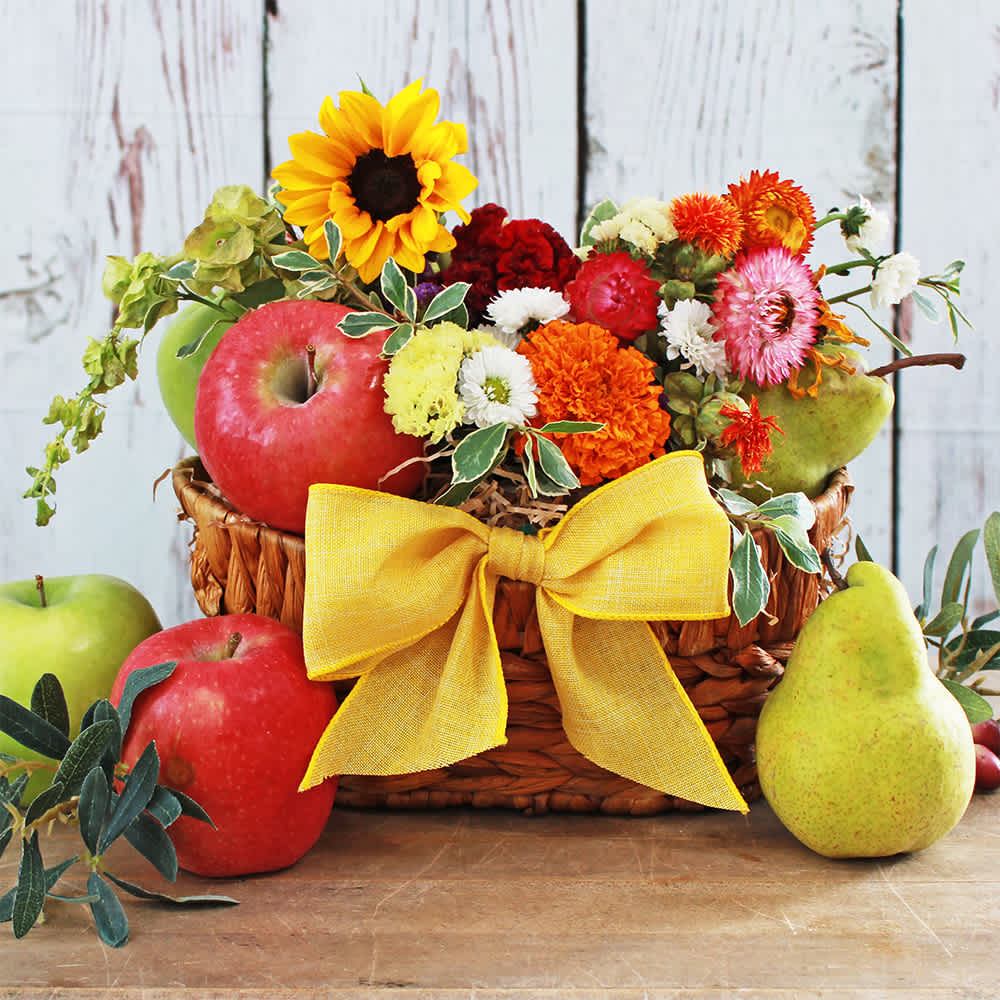 Cheerful Blooms & Fruit Gift Basket Cheerful Blooms & Fruit Gift Basket - A heartfelt gesture to brighten anyone's day. This thoughtful gift features a charming 9" x 5" brown basket adorned with a cheerful yellow ribbon. Inside, you'll find a selection of five fresh fruits, including crisp apples and juicy pears, providing a refreshing treat. Complementing the fruit are seasonal flowers, carefully chosen to match a vibrant color palette. Expect to see a mix of fresh, colorful hand selected seasonal blooms. This gift set is a delightful combination of nature's bounty and floral beauty, perfect for sending your warmest thoughts and best wishes. Contents: yellow ribbon, 5x fresh fruit (apples, pears), *flowers depend on availability/ seasonality but will be a similar color palette. Photo shows a small sunflower, marigold, celosia cockscomb, statice, daisies, strawflowers, safflower, and greenery.