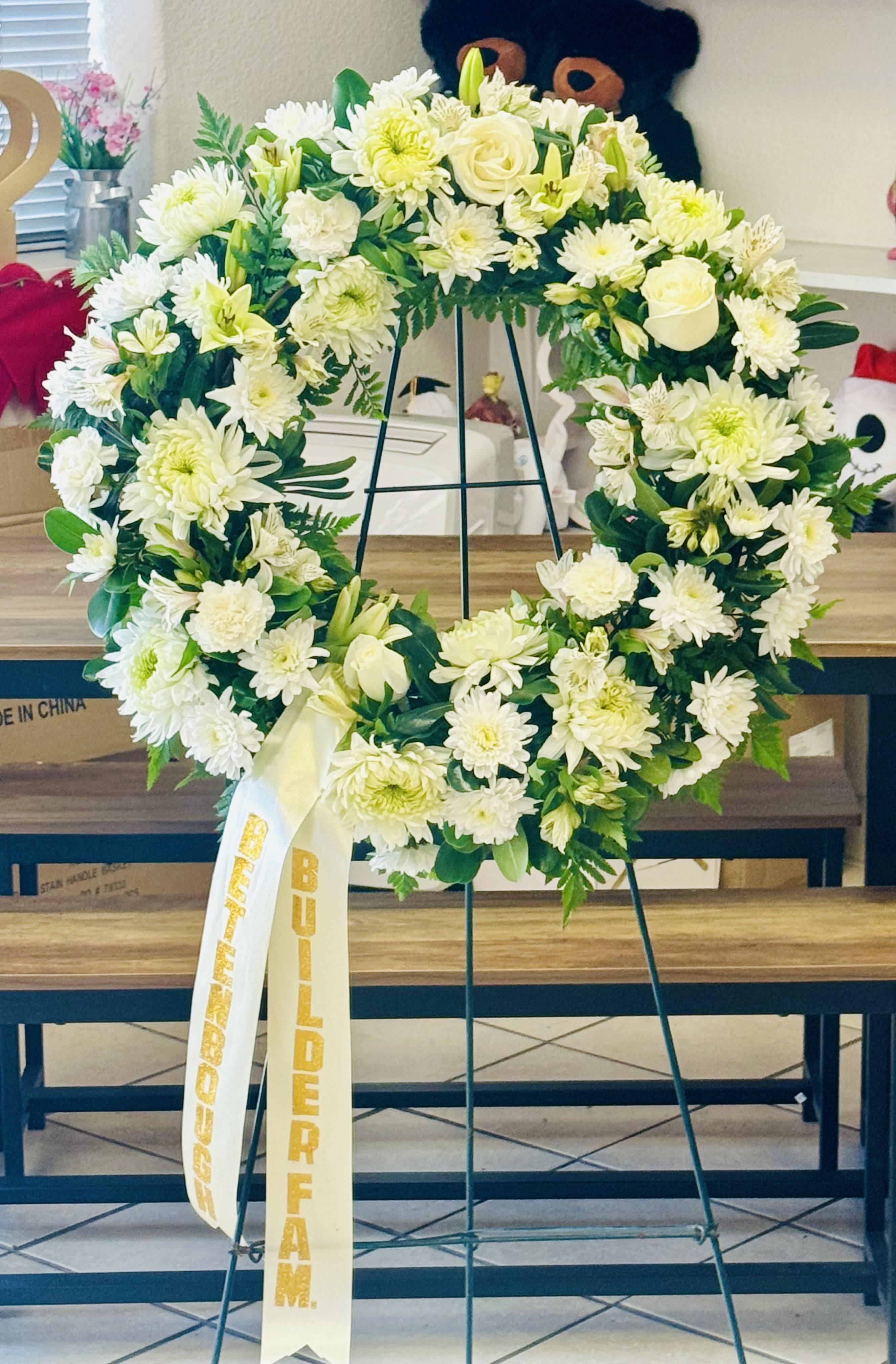 All white standing 18” wreath - A 18” wreath arranged with white florals and greenery. Ribbon with names not included but can be added for 11.99. Upgrades available deluxe and premium 