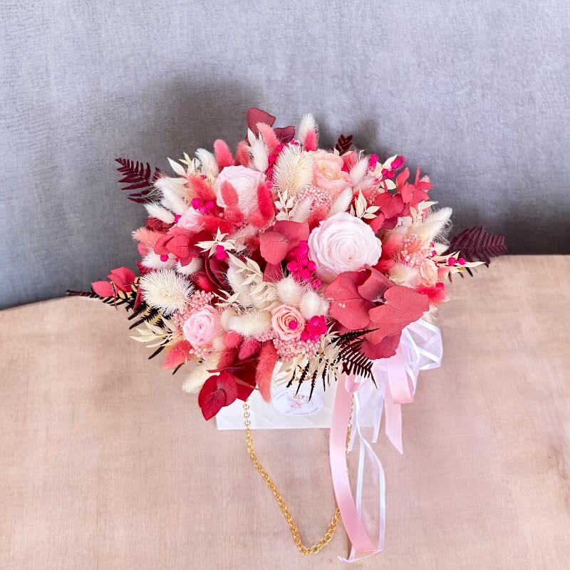 Eternal Elegance Bag #76 - The Eternal Elegance Bag is a sophisticated floral arrangement presented in a luxurious white bag, featuring preserved roses and a curated selection of dried flowers and greenery. Adorned in a harmonious palette of white, pink, and burgundy, this arrangement exudes timeless beauty. Designed to last for years without the need for watering, it offers a lasting symbol of elegance and enduring love. Perfect for any occasion, this maintenance-free masterpiece adds a touch of perennial grace to any space.