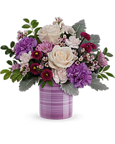 Teleflora's Serene Swirl Bouquet - This Mother's Day, give mom a hand with this hand-painted ceramic vase filled with a beautiful array of creamy roses and lavender blooms. CrÃ¨me roses, purple carnations, miniature light pink carnations, lavender cushion spray chrysanthemums, purple button spray chrysanthemums and pink waxflower are arranged with dusty miller and huckleberry. Delivered in a Serene Swirl vase.
