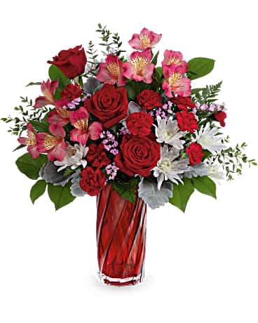 Teleflora's Swirling Splendor Bouquet - Make hearts swirl this Valentine's Day with this romantic bouquet of red roses in a stunning art glass vase with a swirling shape and shimmering pearlescent finish. This bouquet features red roses, pink alstroemeria, miniature red carnations, white cushion spray chrysanthemums, pink sinuata statice, dusty miller, parvifolia eucalyptus, leatherleaf fern and lemon leaf. Delivered in a Swirling Splendor Vase.