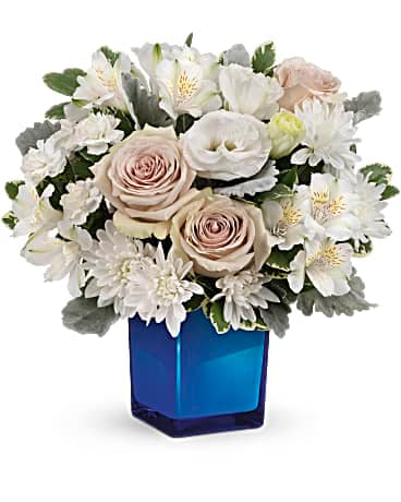 Teleflora's Serene Sky Bouquet - Reminiscent of a romantic walk along the ocean, this beautiful bouquet pairs pale roses with a rich cobalt glass cube vase. Later, your lucky recipient can use it as a comely candleholder! This romantic bouquet features crÃ¨me roses, white cushion spray chrysanthemums, white lisianthus, white alstroemeria, miniature white carnations, dusty miller and variegated pittosporum. Delivered in a Color Splash Cube.