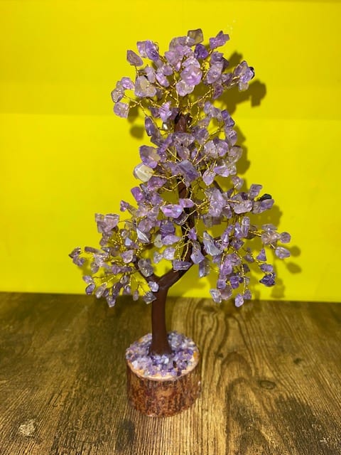 Amethyst Wire Tree Sculpture - Behold the beauty of our Amethyst Wire Tree Sculpture, an exquisite creation standing at approximately 11 inches tall. This unique wire tree combines the artistry of handcrafted design with the calming and spiritual energies of amethyst crystals. Infuse your space with the serene vibes of purple elegance and let the tranquil presence of amethyst enhance your surroundings.  Key Features:  Artisanal Craftsmanship:  Meticulously crafted wire forms the branches, creating an intricate and visually stunning tree sculpture. The artistry behind the design mirrors the grace and fluidity found in nature, capturing the essence of a flourishing tree. Amethyst Crystals:  Amethyst, renowned for its soothing purple hues, graces the branches, radiating a tranquil and spiritually uplifting energy. The crystals are carefully selected for their clarity and beauty, enhancing the overall aesthetic and energetic qualities. Approximate Height of 11 inches:  Standing at an approximate height of 11 inches, the sculpture is a versatile and impactful addition to tabletops, shelves, or any space seeking a touch of purple serenity. Calming and Spiritual Energies:  Amethyst is known for its ability to promote calmness, enhance spiritual awareness, and provide a sense of tranquility. The tree's design serves as a symbolic representation of growth and inner peace, amplifying the calming energies of amethyst. Symbol of Harmony:     