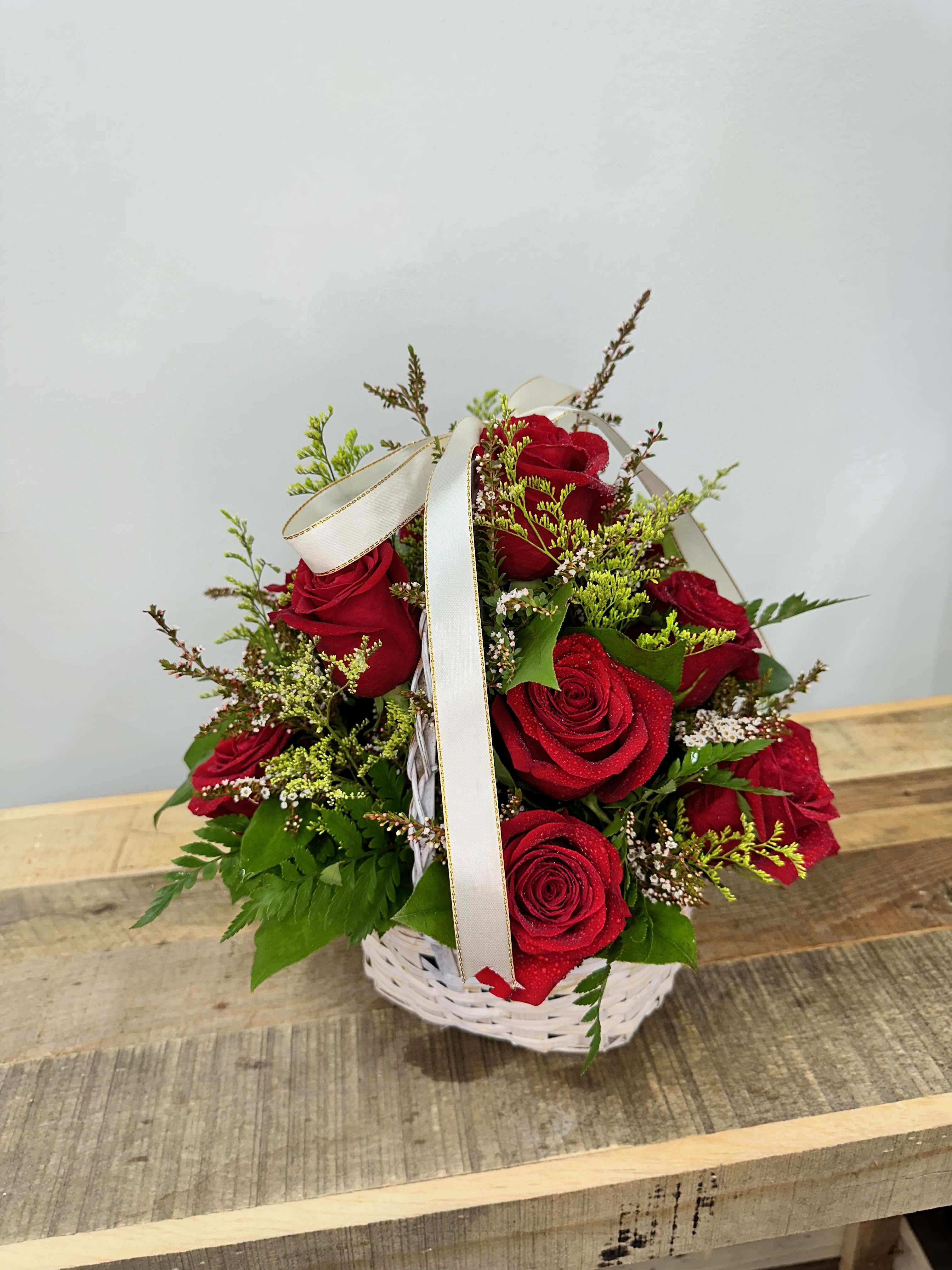Red Riding Basket -  This arrangement of deep red roses nestled in a white basket, accented with lush greenery. This enchanting bouquet captures the essence of timeless love and adventure, perfect for bringing a touch of storybook romance to any occasion.