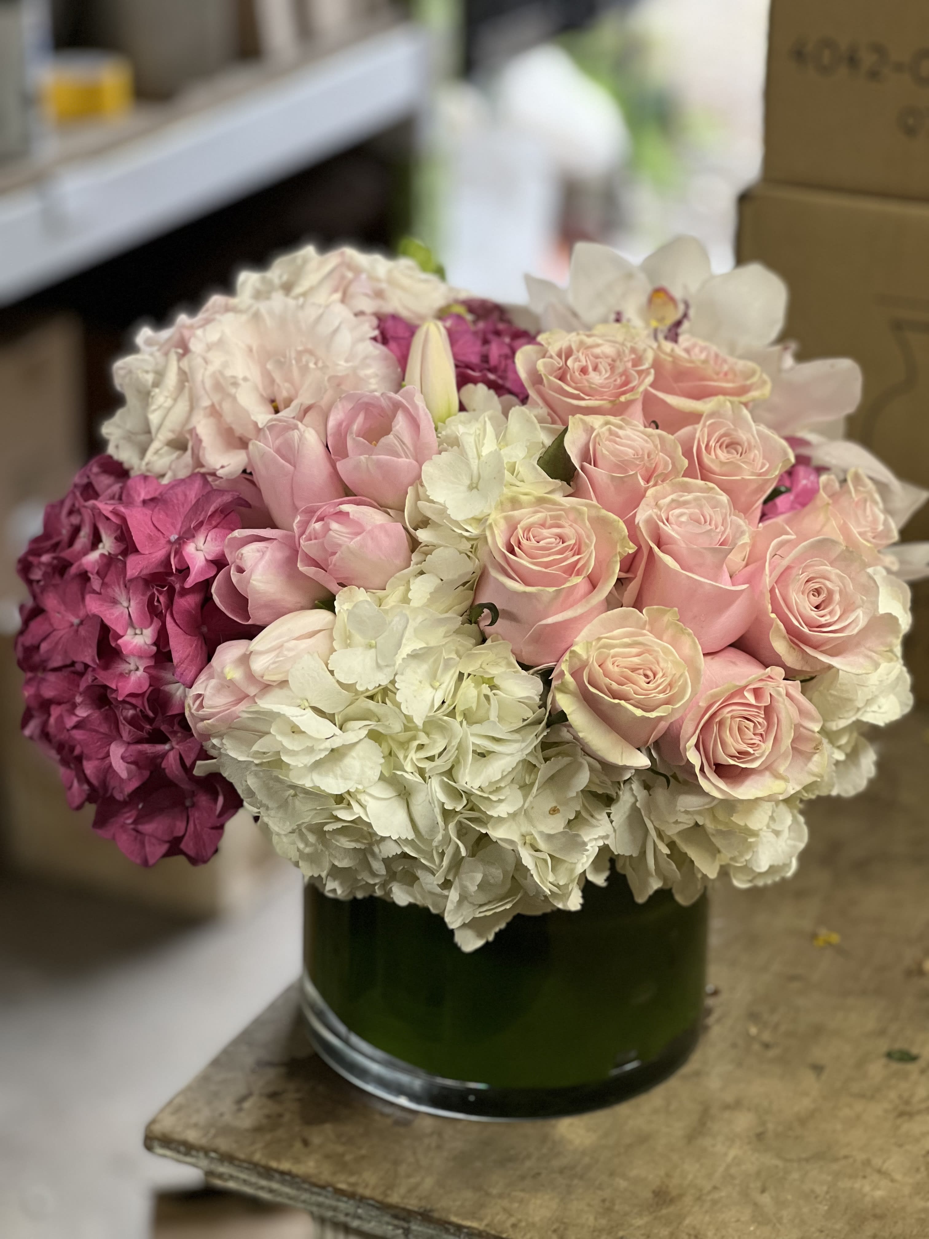 PINKS AND CREAM - A luxurious, mix of roses, hydrangea, tulips and exotic Cymbidium Orchid blooms it is  bursting with flowers in calming shades. Designed in a beautiful leaf lined glass vase for a modern touch of elegance.  NEED A TIMED DELIVERY? If you require an order to be delivered within a 3 hour window you MUST add our “Rush Delivery.” Specify your 3 hour window request in “Florist instructions” during the checkout process. (All deliveries are made between 9 a.m. and 4 p.m. only)