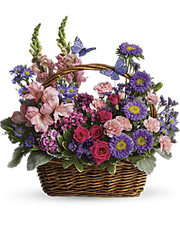 Country Basket Blooms - Take a walk through a country meadow with this fresh flower basket! Pretty blooms of pink and purple nestle happily inside a natural gift basket as playful purple butterflies flutter overhead. Fresh flowers including snapdragons, alstroemeria, mini carnations and matsumoto asters are assembled in a natural basket with decorative butterflies. Orientation: One-Sided