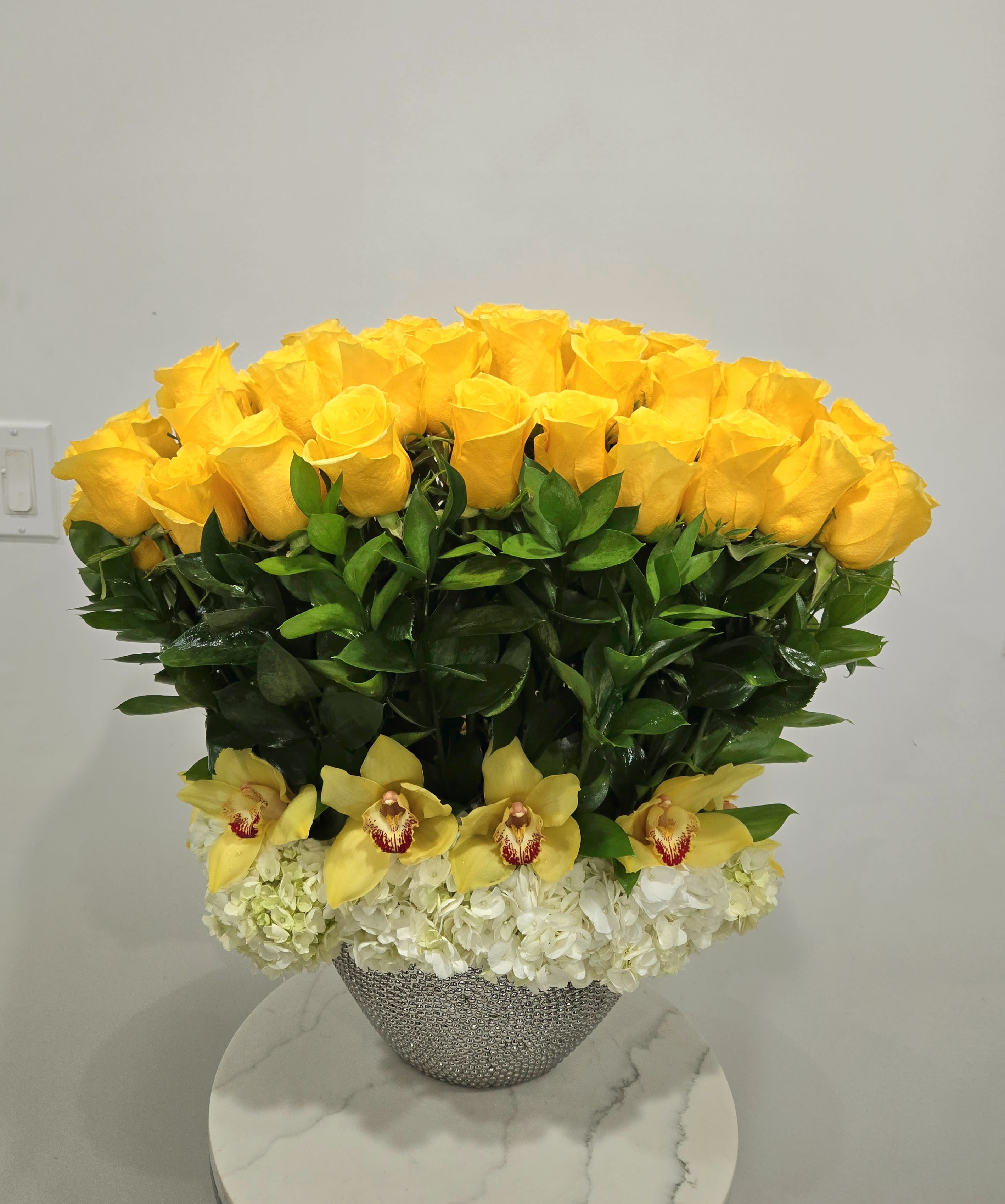 Light of Day - A stunning and modern arrangement of yellow roses that can be created in any color roses. The roses are designed with hydrangeas and cymbidium orchid blooms in a silver oval container.