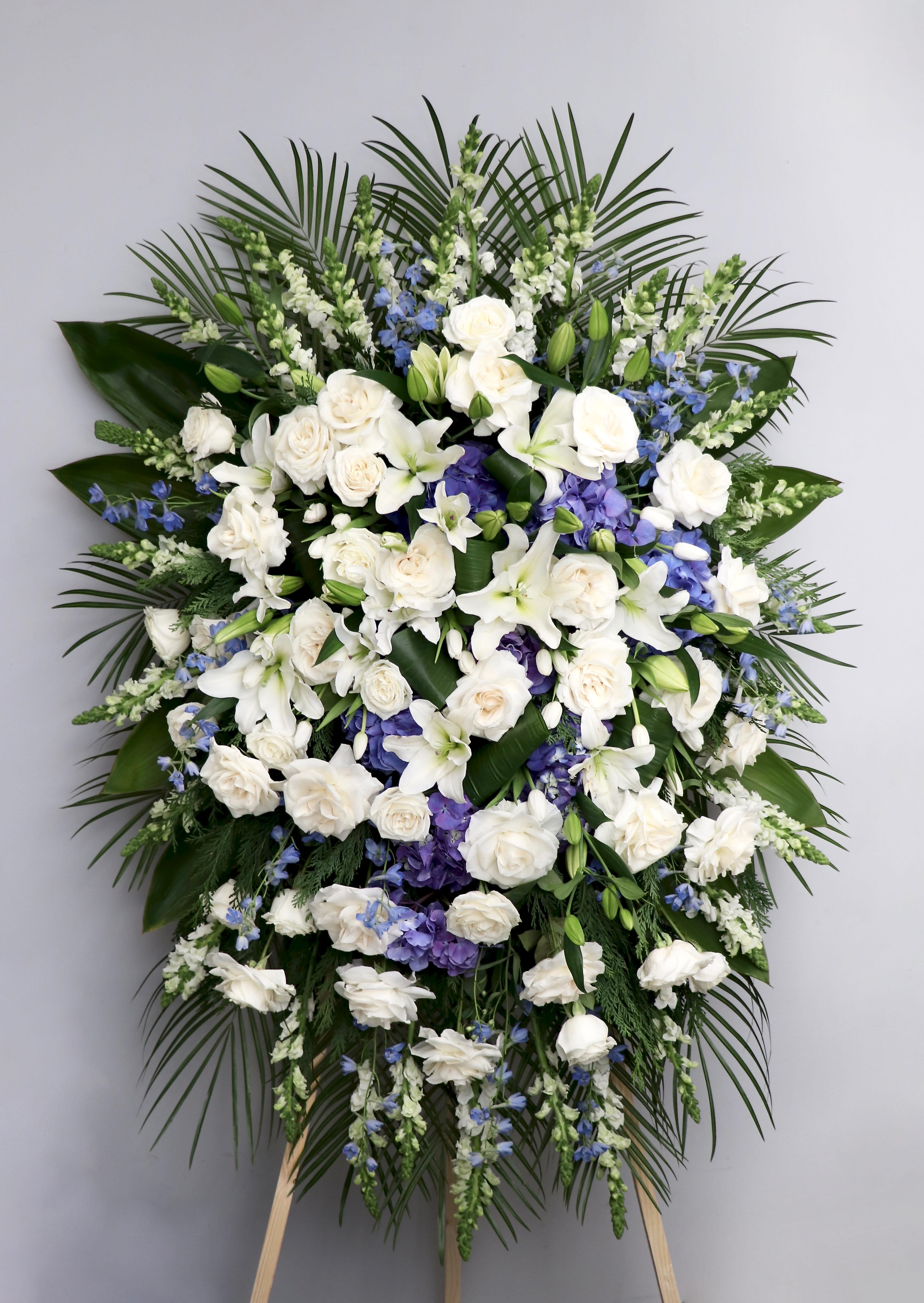 Lily, Rose, and Delphinium Spray  - This spray is made with white roses and lilies with blue delphiniums for a lovely touch of color.    We include easel, printed banner and delivery (some fees may apply). An additional banner can be added for $15.  Standard size is 30'' wide, deluxe is 36'', and premium is 42''.