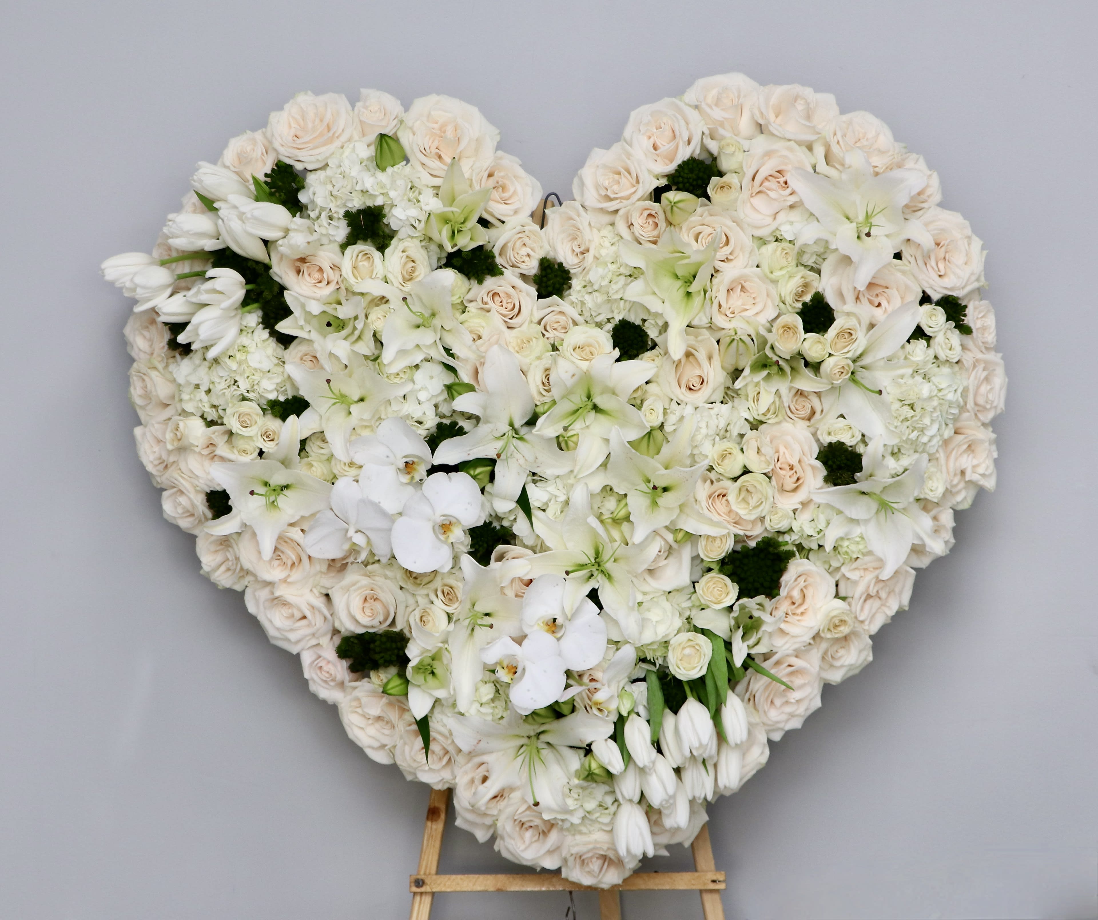 White and Green Orchid Heart - This white and green heart contains a beautiful mix of orchids, stargazer lilies, roses, and seasonal greens.     Three sizes are available, measuring approximately 30 inches for standard, 36 inches for deluxe, and 42 inches for premium. Additional flowers will also be added to deluxe and premium sizes.     We include easel, printed banner, and delivery (some fees may apply). An additional banner can be added for $15