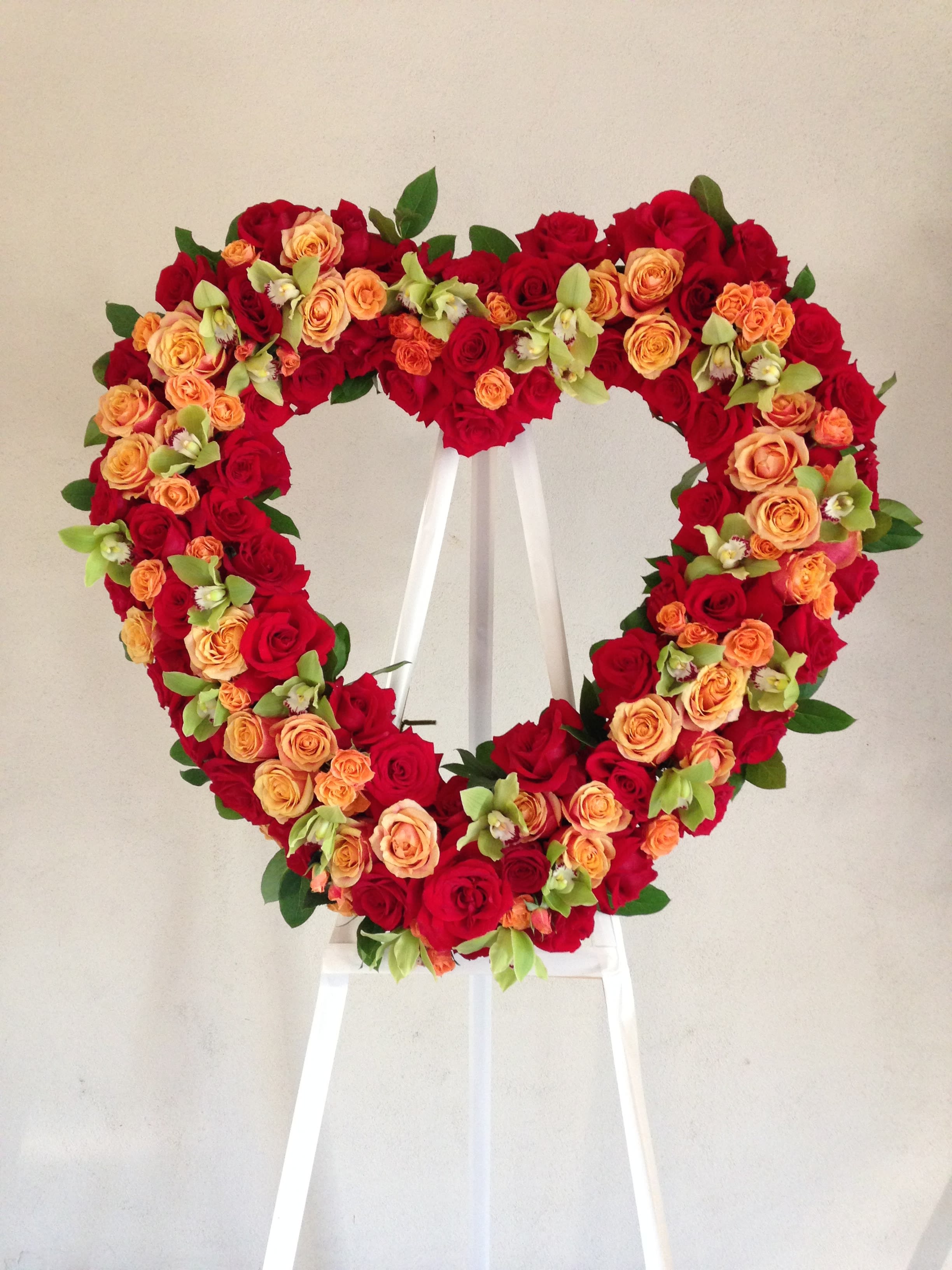 Red and Orange Roses With Orchids Heart  - This heart contains red and orange roses, orchids, and minimal seasonal greens.     We include easel, printed banner and delivery (some fees may apply). An additional banner can be added for $15    Standard size is 30'', deluxe is 36'', and premium is 42''.  
