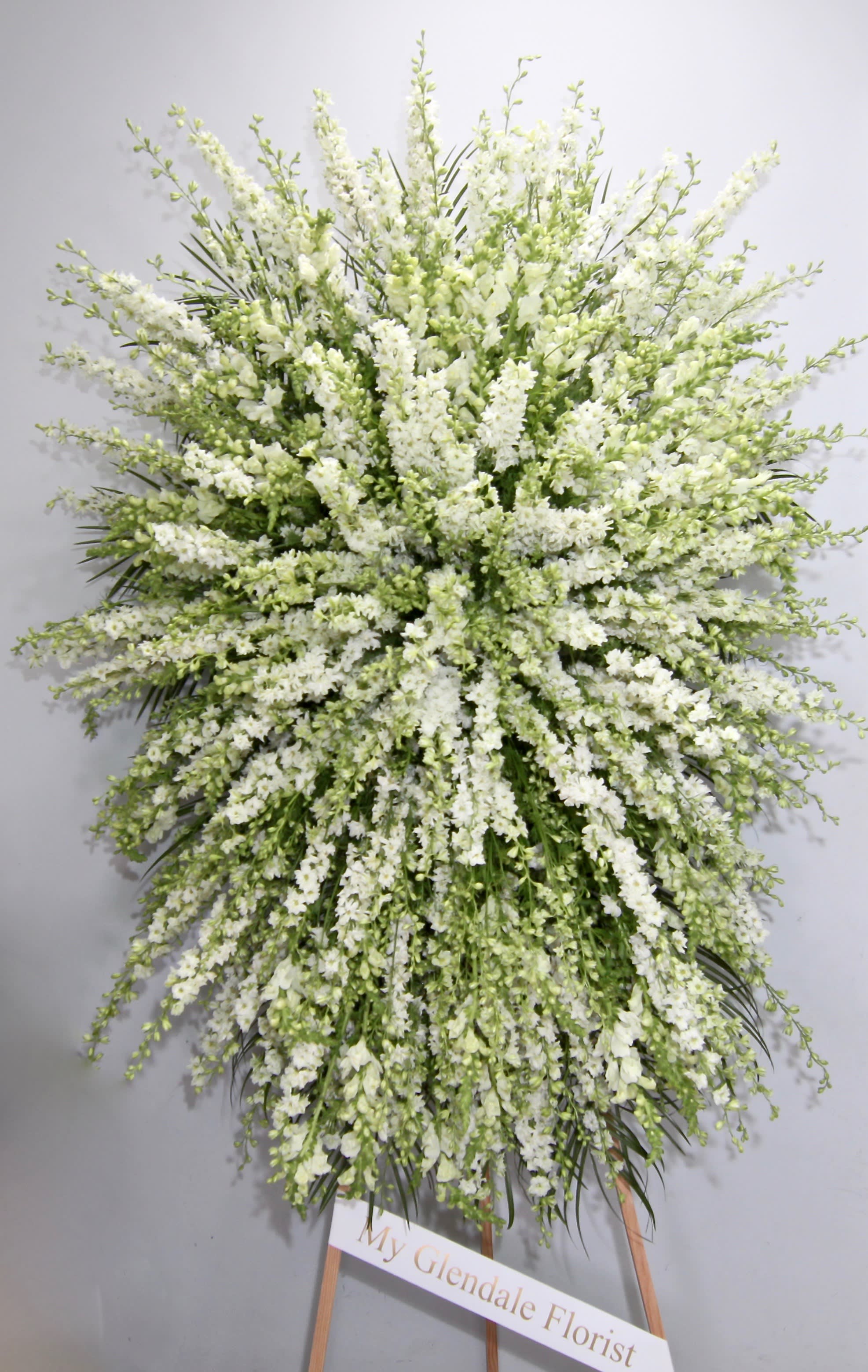 Million Little Stars Spray  - This sympathy spray is made with an elegant combination of white snapdragons and seasonal florals.    We include easel, printed banner and delivery (some fees may apply). An additional banner can be added for $15.    Standard size is 30'' wide, deluxe is 36'', and premium is 42''.