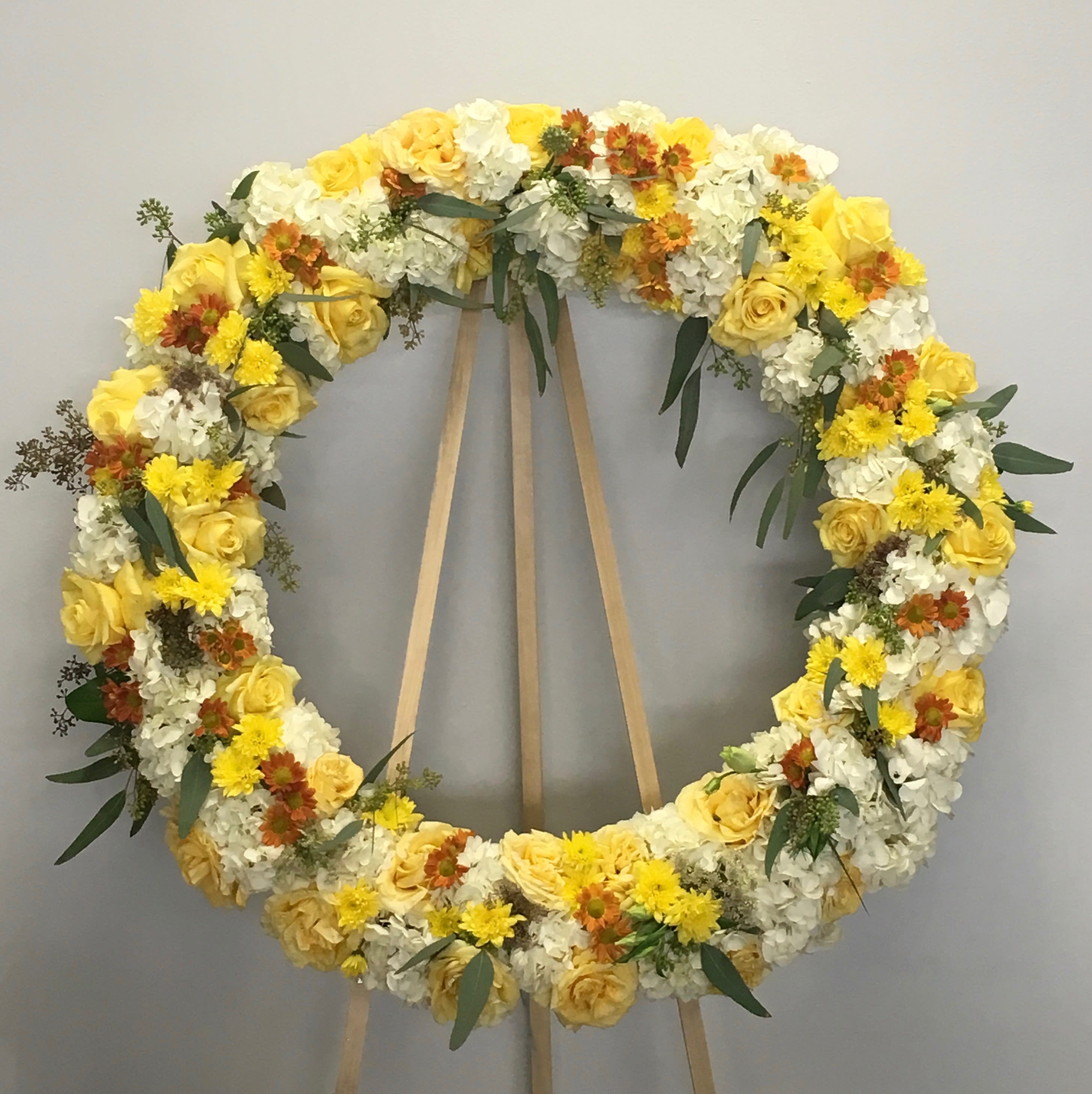 Sunshine Days Wreath  - This wreath includes a bright mix of roses, hydrangeas, seasonal florals and greens.     We include easel, printed banner and delivery (some fees may apply). An additional banner can be added for $15    Standard size is 30'', deluxe is 36'', and premium is 42''.
