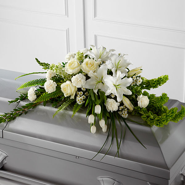 Resurrection Casket Spray 0120 - The Resurrection Casket Spray inspires thoughts of comfort and peace to those wishing to pay their respects for the loss of the deceased. White tulips roses snapdragons Oriental lilies larkspur carnations and monte casino asters are accented by the bright green stems of Bells of Ireland and an assortment of the finest lush greens to create the perfect arrangement to display on the top of their casket during their final farewell service.