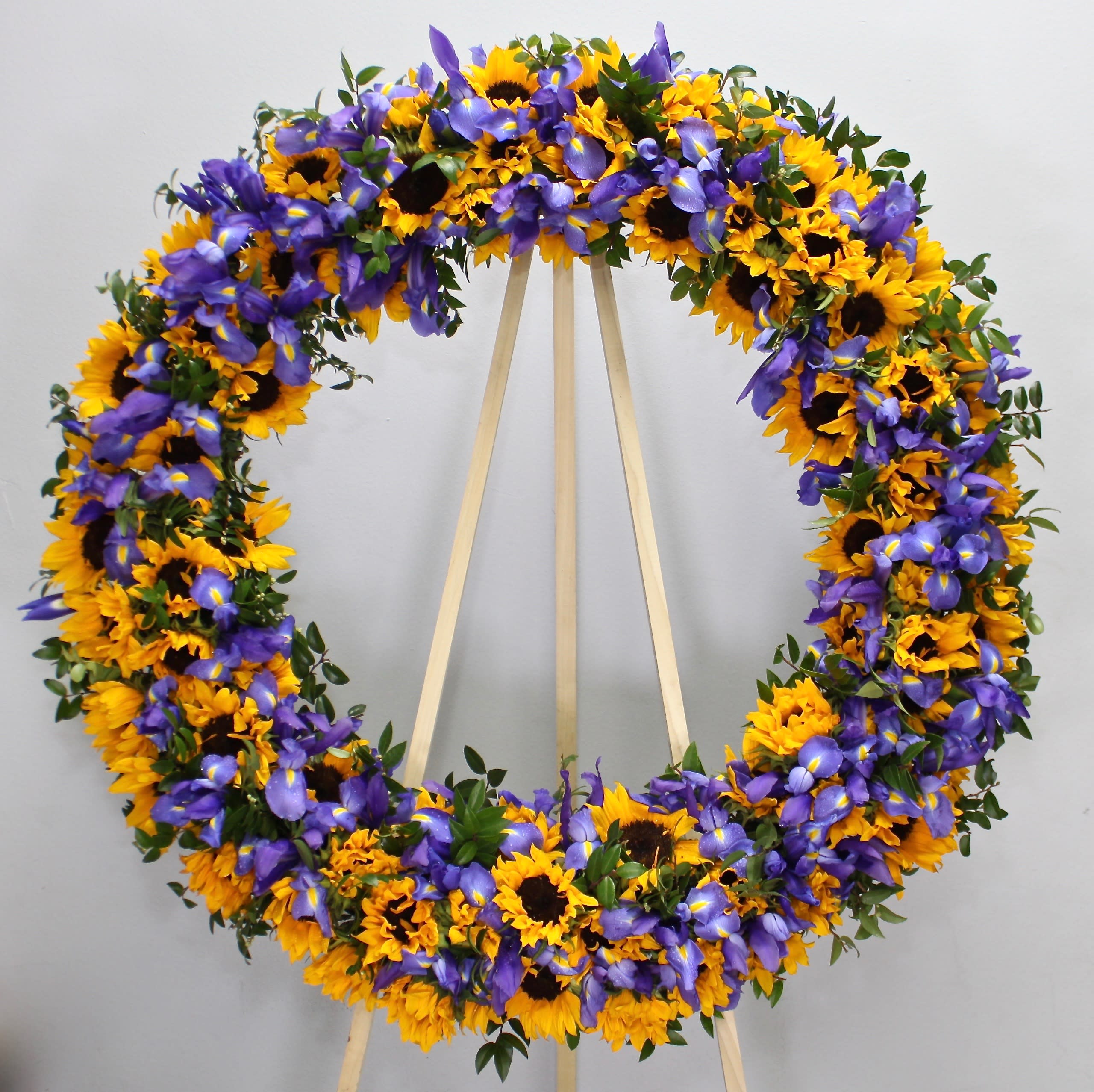 Sunflower Summer Wreath  - This sympathy spray contains a mix of sunflowers, seasonal purple flowers, and greens.     We include easel, printed banner and delivery (some fees may apply). An additional banner can be added for $15    Standard size is 30'', deluxe is 36'', and premium is 42''.