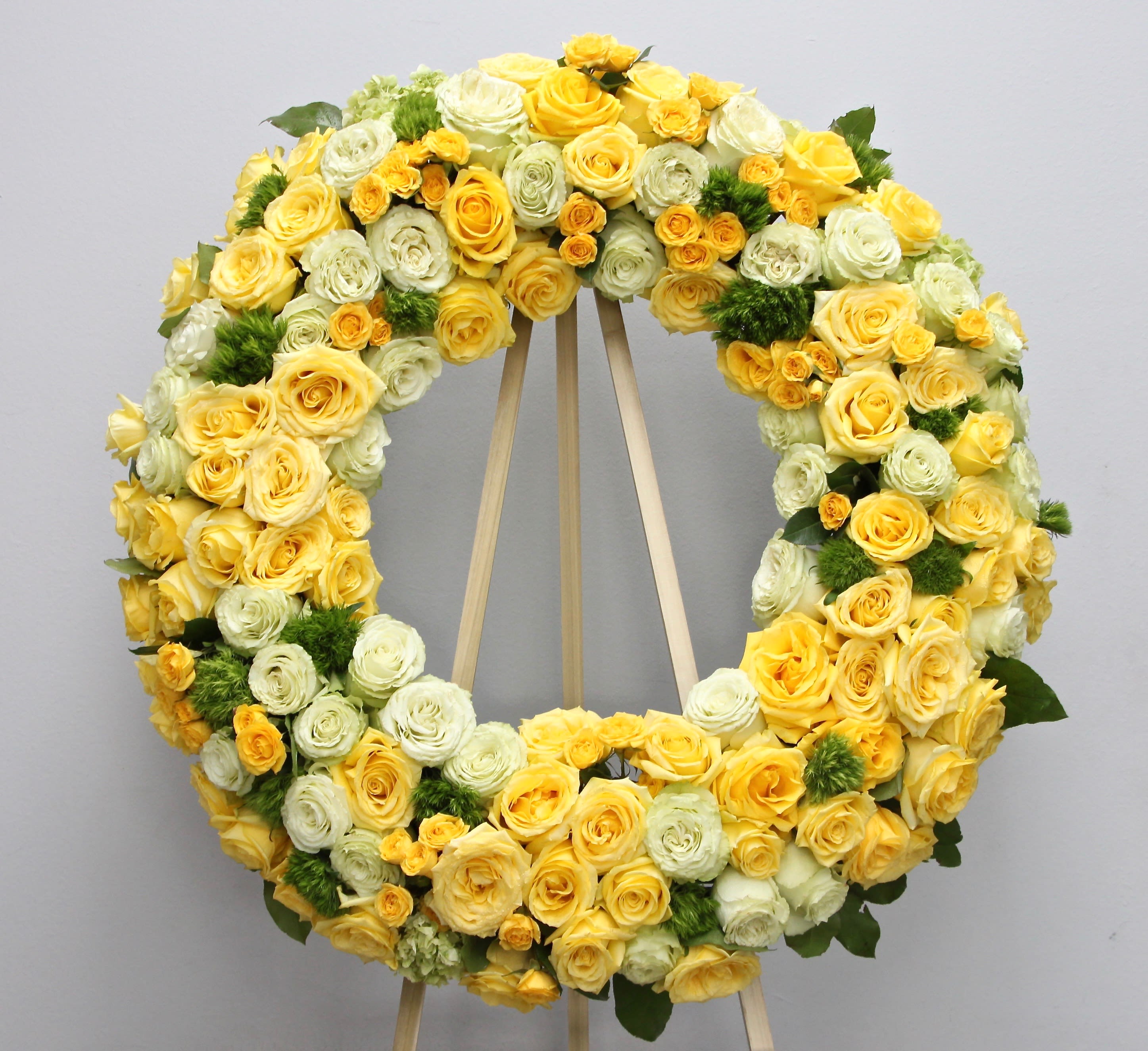 Sunshine Wreath  - This sympathy spray includes bright yellow roses, hydrangeas, and fluffy seasonal greens.     We include easel, printed banner and delivery (some fees may apply). An additional banner can be added for $15    Standard size is 30'', deluxe is 36'', and premium is 42''.