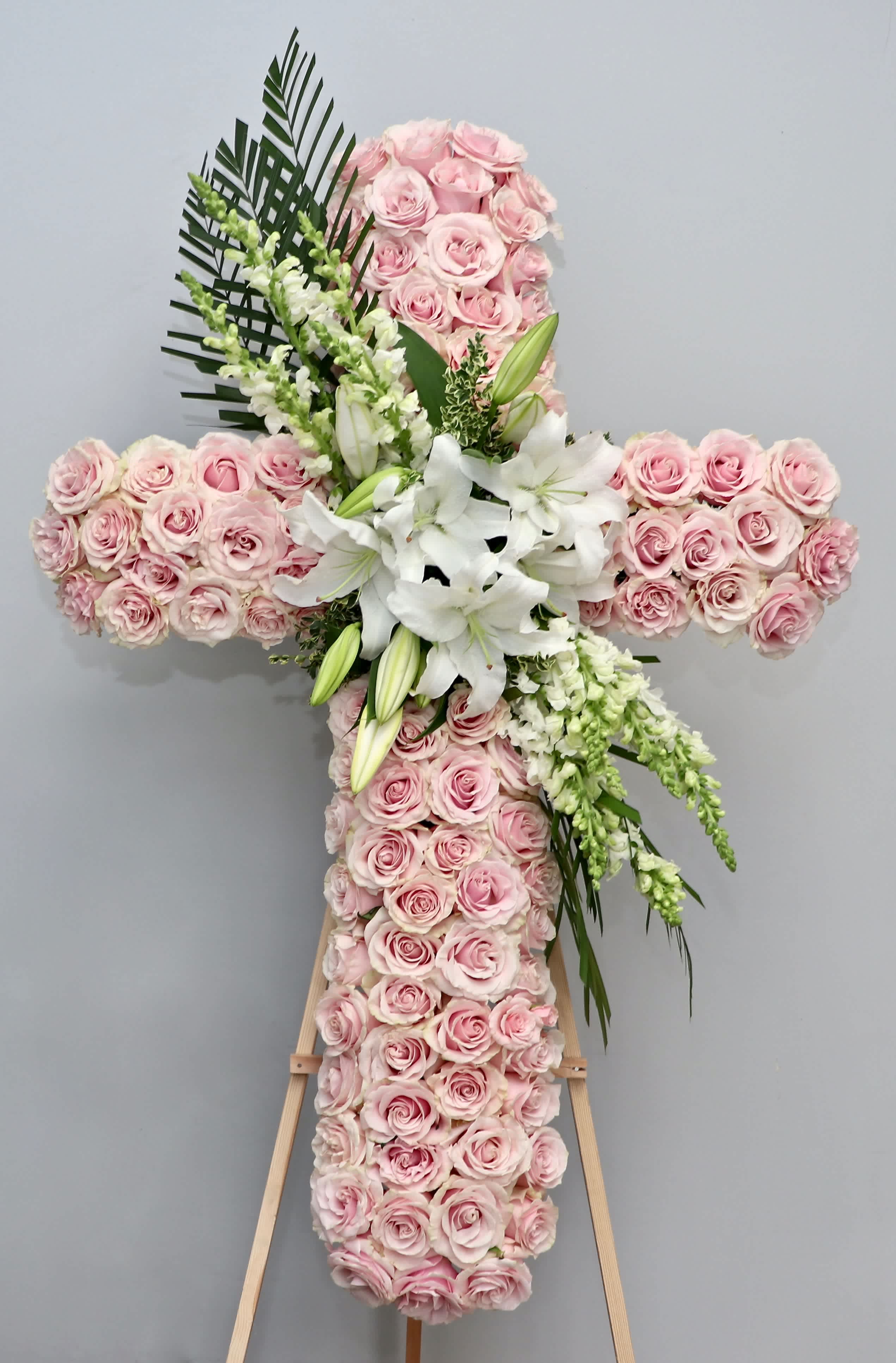 Blush Pink Cross  - This beautiful sympathy cross is carefully arranged with pink roses, snapdragons, and lilies.    We include easel, printed banner and delivery (some fees may apply). An additional banner can be added for $15.    Standard size is 30'', deluxe is 36'', and premium is 42''.