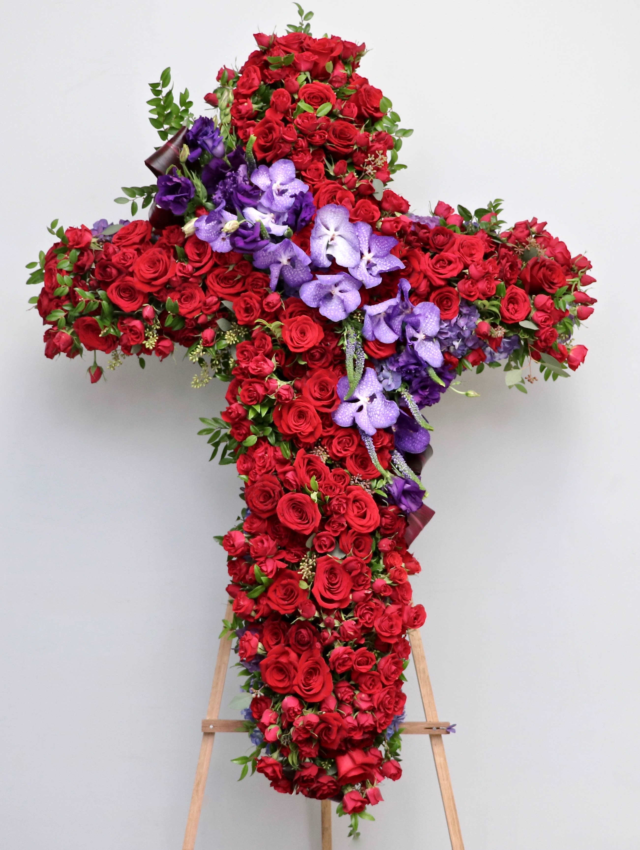 Red and Purple Cross  - This sympathy cross contains vibrant red roses and purple orchids with touches of seasonal greenery.     We include easel, printed banner, and delivery (some fees may apply). An additional banner can be added for $15.    Standard size is 30'', deluxe is 36'', and premium is 42''.