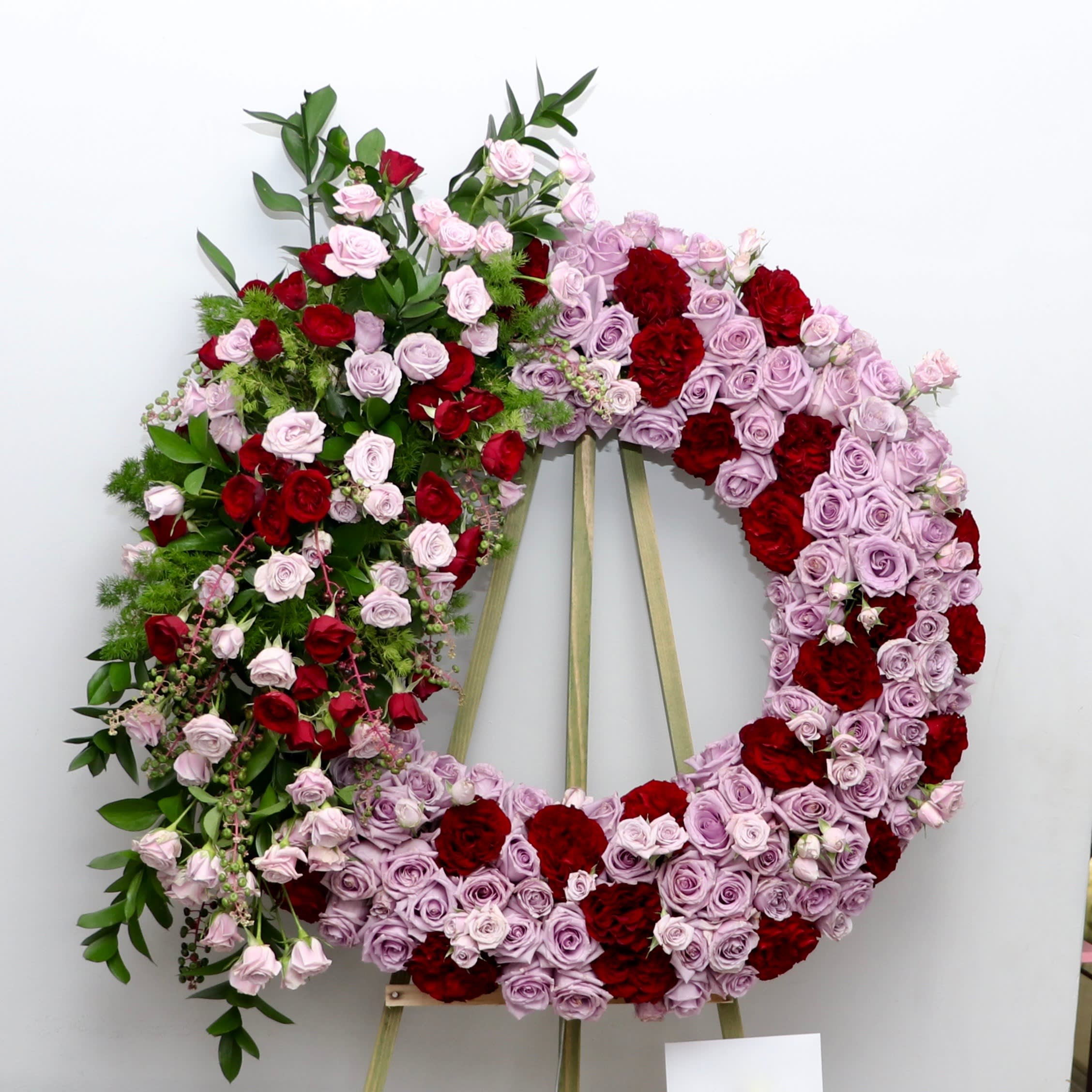 Lavender Memories Lavender Memories - This sympathy wreath includes soft lavender roses with pops of red and seasonal greenery. We include easel, printed banner and delivery (some fees may apply). An additional banner can be added for $15 Standard size is 30'', deluxe is 36'', and premium is 42''.