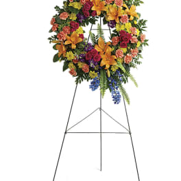 Colorful Serenity Wreath - Like a beacon of love and hope, this glorious wreath of hydrangea, roses and lilies echoes the joy of your precious memories.   •This wreath features green hydrangea, hot pink spray roses, orange asiatic lilies, orange carnations, blue delphinium, purple stock, yellow cushion spray chrysanthemums, huckleberry, variegated pittosporum, sword fern, silver dollar eucalyptus, and lemon leaf.