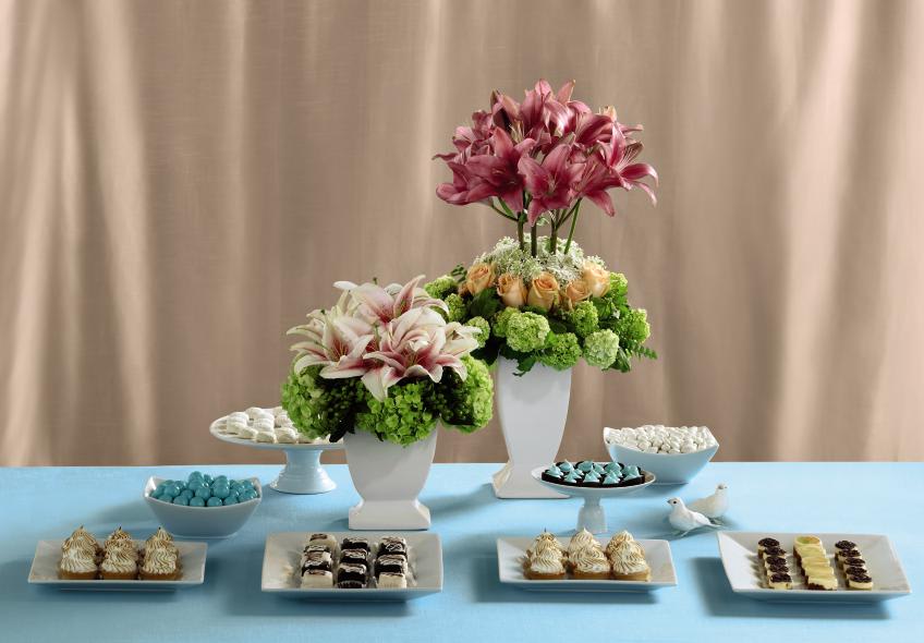 FTD Life's Sweetness Centerpiece - The FTD Life's Sweetness Centerpiece is a fantastic display of  innovative design. Featuring two different arrangements, each set in  white ceramic vases varying in height, this centerpiece creates a  whimsical presentation perfect for your dessert table at the reception.  The first bouquet highlights the beauty of Stargazer Lilies by centering  them within the arrangement and surrounding them with green hydrangea  and hypericum berries. The second bouquet has a topiary feel towards it  as beautiful pink Asiatic Lilies reach for the sky stemming from a  compact arrangement of peach roses, green viburnum and Queen Anne's  Lace. Shorter Arrangement Approx. 15âH x 13âW . Taller Arrangement  Approx.  26H x 15W.  