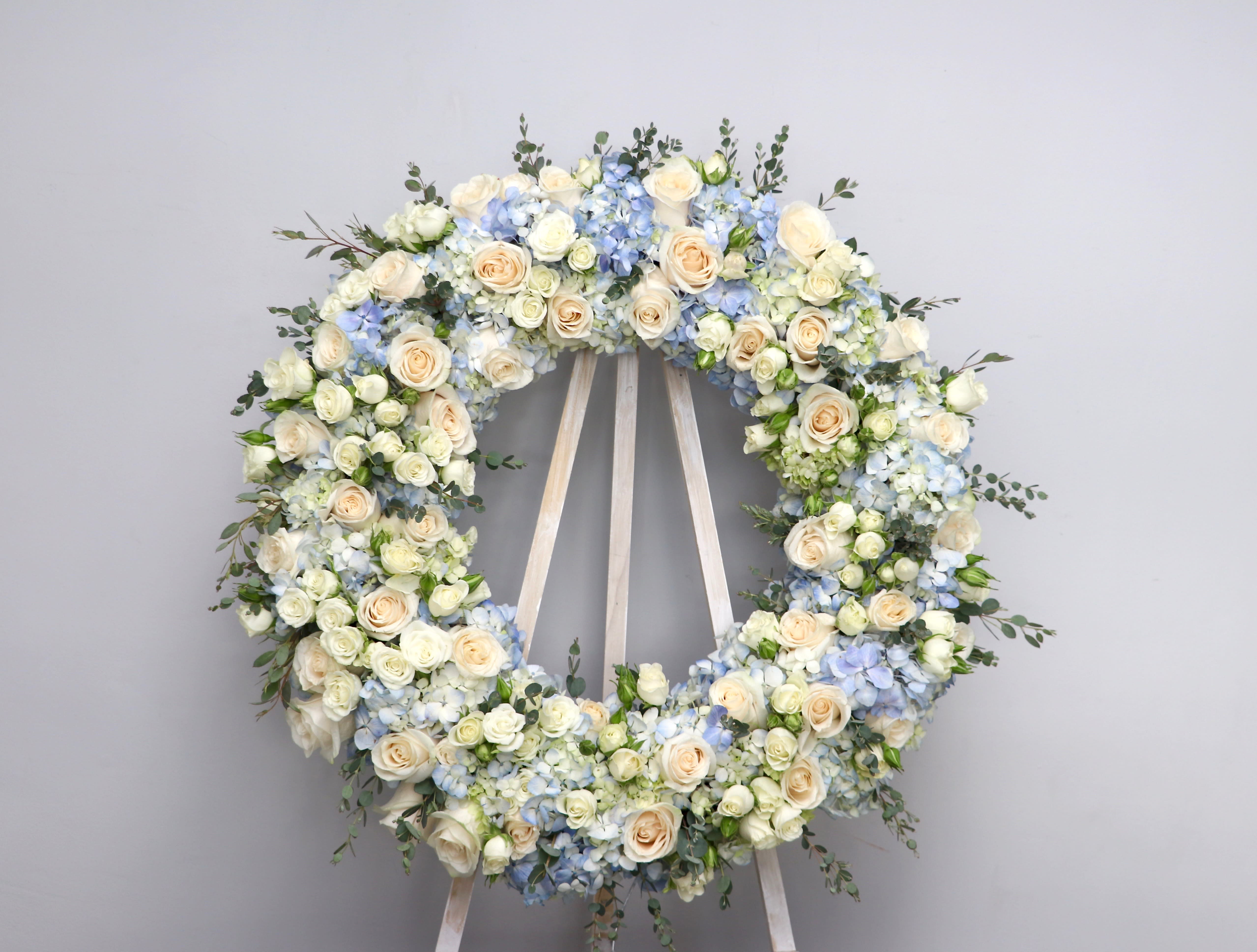 Soft Blue Wreath  - Baby blue hued florals to fill this wreath.    We include easel, printed banner and delivery (some fees may apply). An additional banner can be added for $15    Standard size is 30'', deluxe is 36'', and premium is 42''.