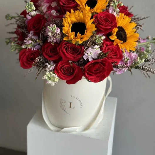 Sunset Romance - A captivating arrangement that combines the rich, romantic allure of red roses with the cheerful brightness of sunflowers, complemented by a mix of complementary blooms. All beautifully arranged in a pristine white box, this bouquet captures the essence of a sunset’s warm embrace, bringing a touch of elegance and joy to any occasion.