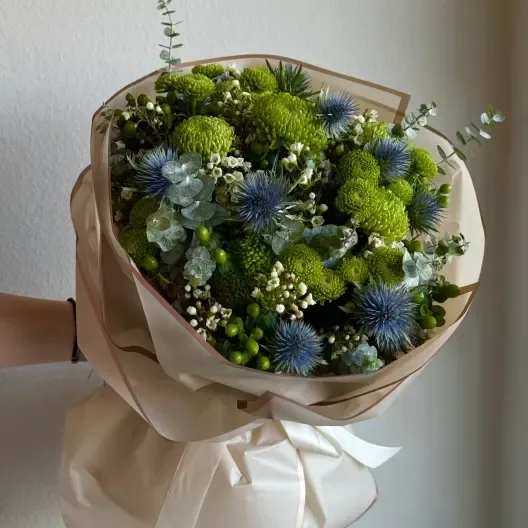 Thistle Bouquet - A captivating handheld bouquet showcasing the unique beauty of blue thistles paired with a vibrant mix of lush greens. This arrangement exudes a whimsical, wild charm, perfect for adding a touch of nature’s untamed elegance to any occasion.