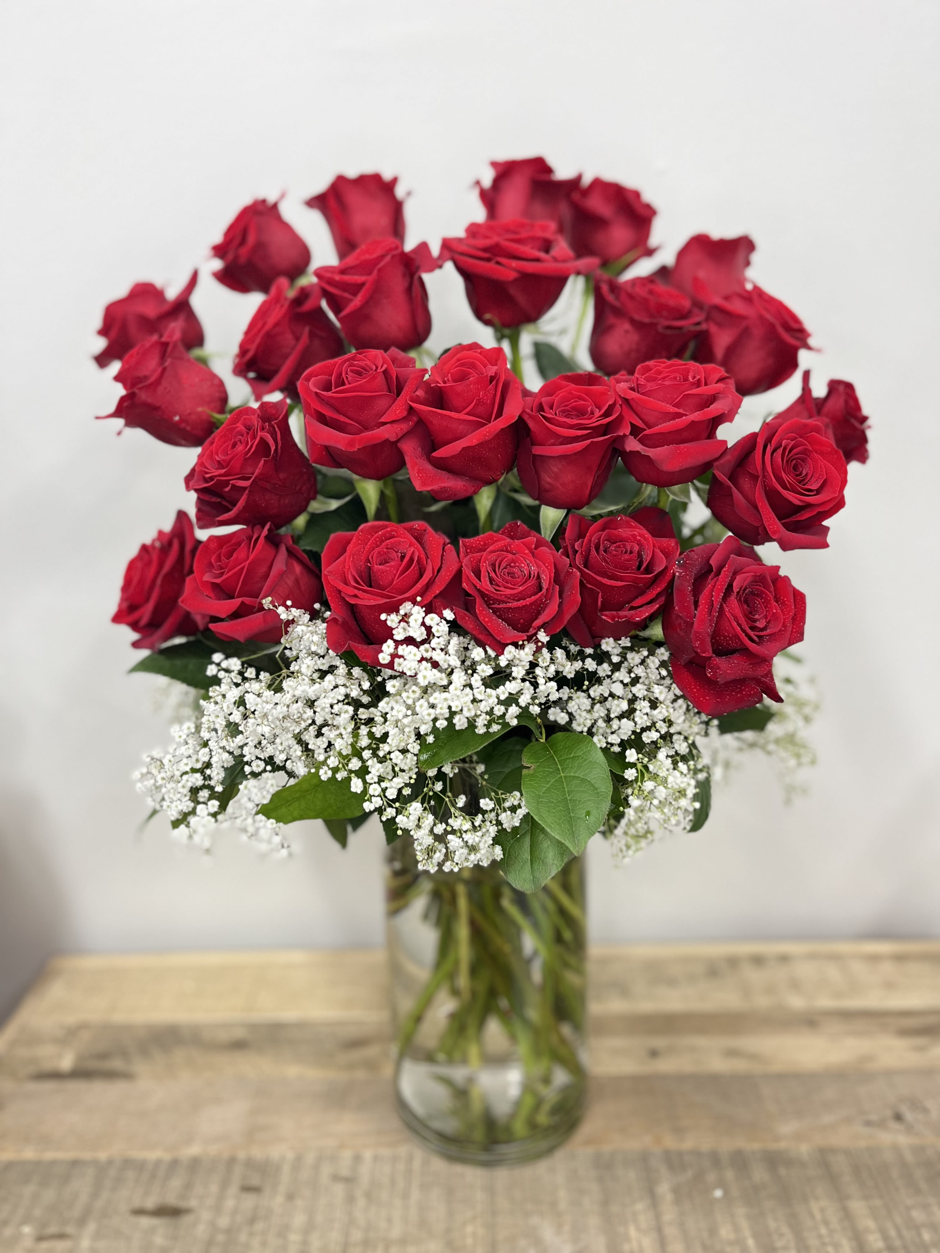 Single Sided Splendor - Our &quot;Single-Sided Splendor&quot; features 25 vibrant red roses arranged to face forward, complemented by lush greenery and delicate baby’s breath.