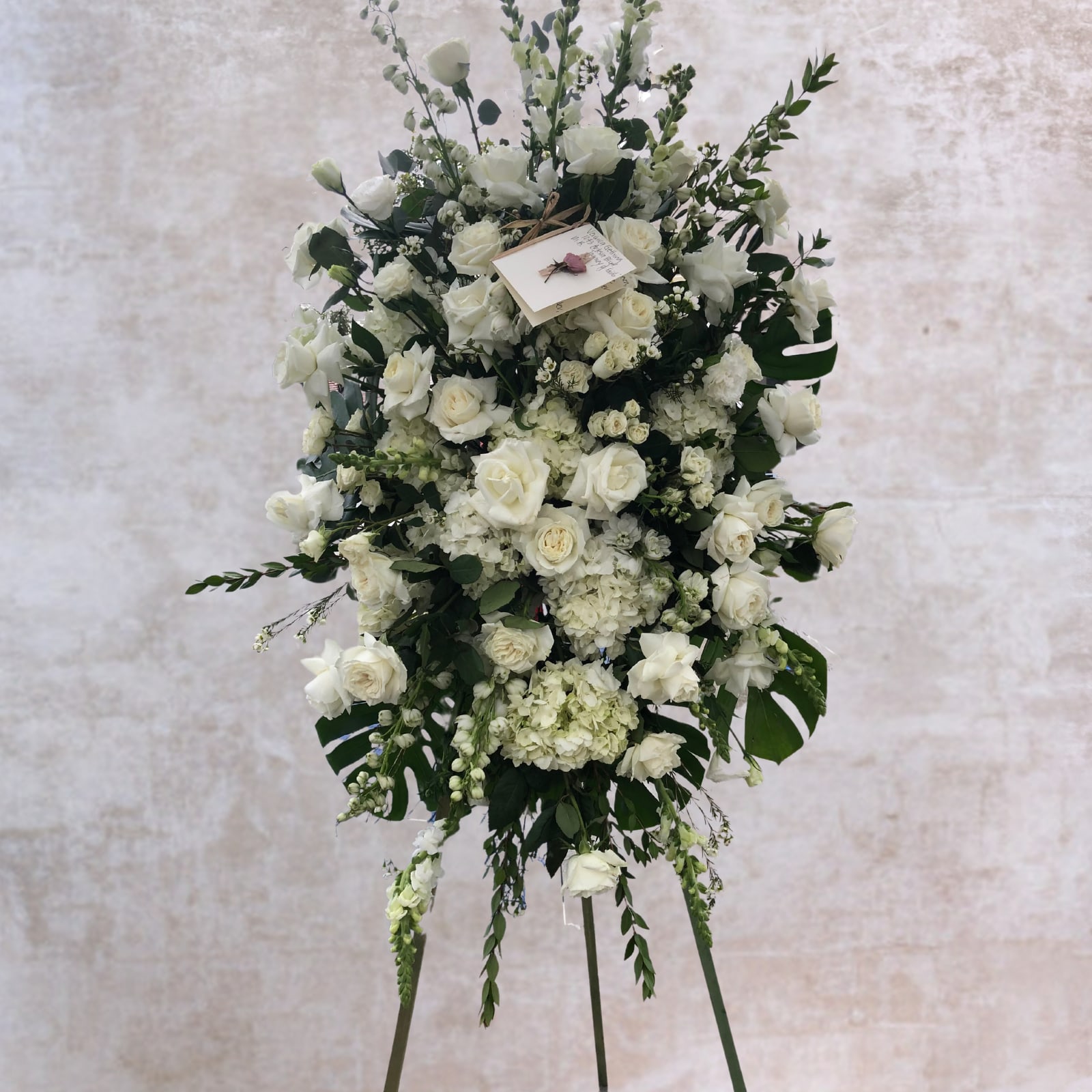 White Bloom Standing Spray with Easel - This standing spray includes a variety of the most beautiful white blooms featuring roses, hydrangeas and snapdragons. Sincerely express your love and remembrance of a beloved life lost and express your sentiments of adoration and wishes for peace with this stunning spray. Includes wood easel for display.  Please call 310-545-4432 if you would like to make any changes. Changes may incur additional charges.