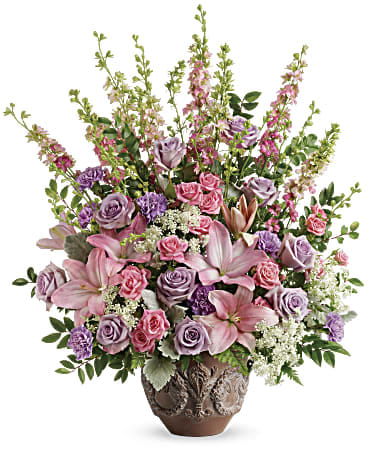 Soft Blush Bouquet  - Like a whisper from heaven, the soft pinks and lavenders in this feminine arrangement bring peace and hope in a time of loss. Presented in a large antiqued pot, it's a loving tribute all will appreciate.         •This soft pink arrangement features lavender roses, pink spray roses, pink asiatic lilies, lavender carnations, pink larkspur, queen anne's lace, huckleberry, dusty miller, and leatherleaf fern.  