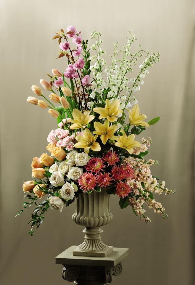 Colorful Altar Arrangmeent Colorful Altar Arrangmeent - This Altar Arrangement blooms with the colors of happiness and grace to celebrate your wedding day. Peach tulips, peach roses, white roses, peach stock, dark pink dahlias, white delphiniums, pink spray roses, peach Asiatic Lilies, pink flowering branches and an assortment of fresh, lush greens are beautifully arranged in a resin urn and displayed on a 3-inch pedestal to brighten the alter during your ceremony. Approx. 48âH x 30âW.