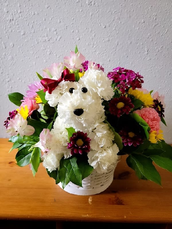 Teacher's Pet - Get ready to go back to school with our &quot;Teacher's Pet&quot; floral creation! This adorable arrangement is hand-designed in the shape of a dog, complete with eyes, nose, and a stylish collar. Made with the freshest carnations, Viking poms, asters, statice, solidago, waxflower, button poms, and monte casino, this bouquet is sure to bring a smile to any teacher’s face. And the best part is It comes in a handsome, reusable handled willow basket, perfect for adding some charm to the classroom. Show your appreciation for the hardworking teachers in your life with this fun and original gift.