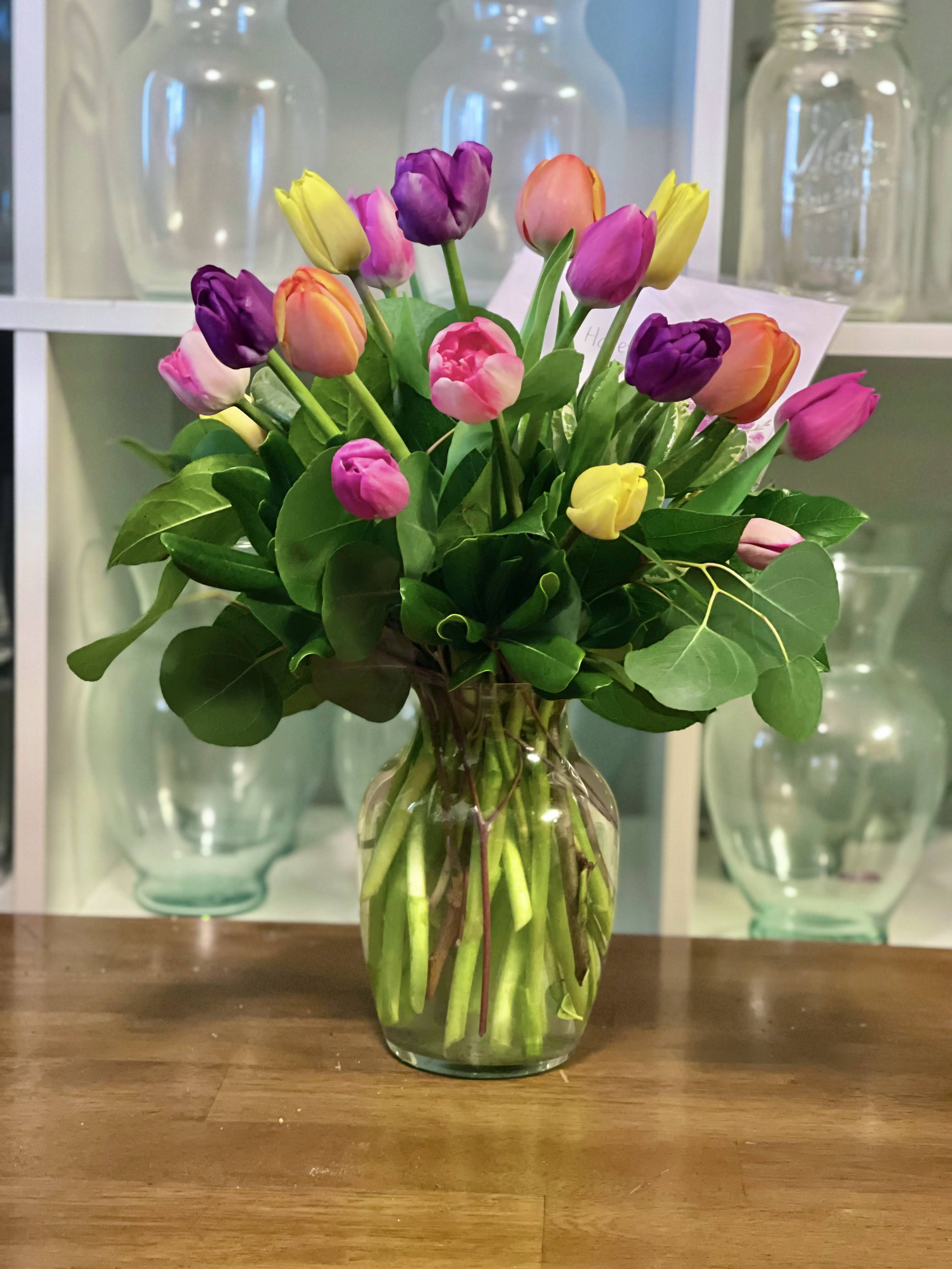 Rainbow Tulips Rainbow Tulips - A colorful blend of tulips with fresh greenery in a clear glass vase.