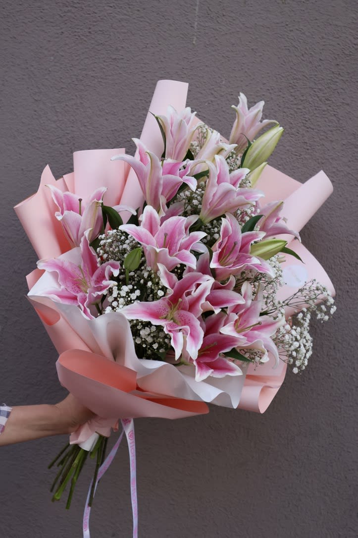 Pink Lilly - A bouquet featuring pink lilies and baby's breath is a classic and timeless arrangement that exudes grace and elegance. The soft, delicate pink hues of the lilies combined with the delicate white blooms of the baby's breath create a romantic and feminine atmosphere, making it perfect for weddings, anniversaries, or as a gesture of love.  