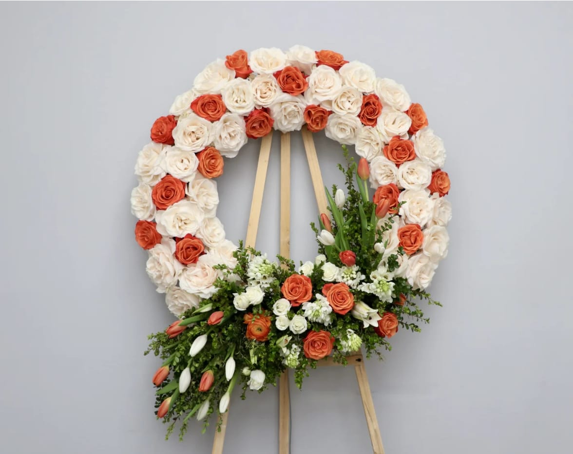 Orange Cream Wreath  - This wreath is made with creamy white roses and touches of orange flowers rose and tulips.    Standard size is 30'', deluxe is 36'', and premium is 42''.  We include easel, printed banner and delivery (some fees may apply). An additional banner can be added for $15