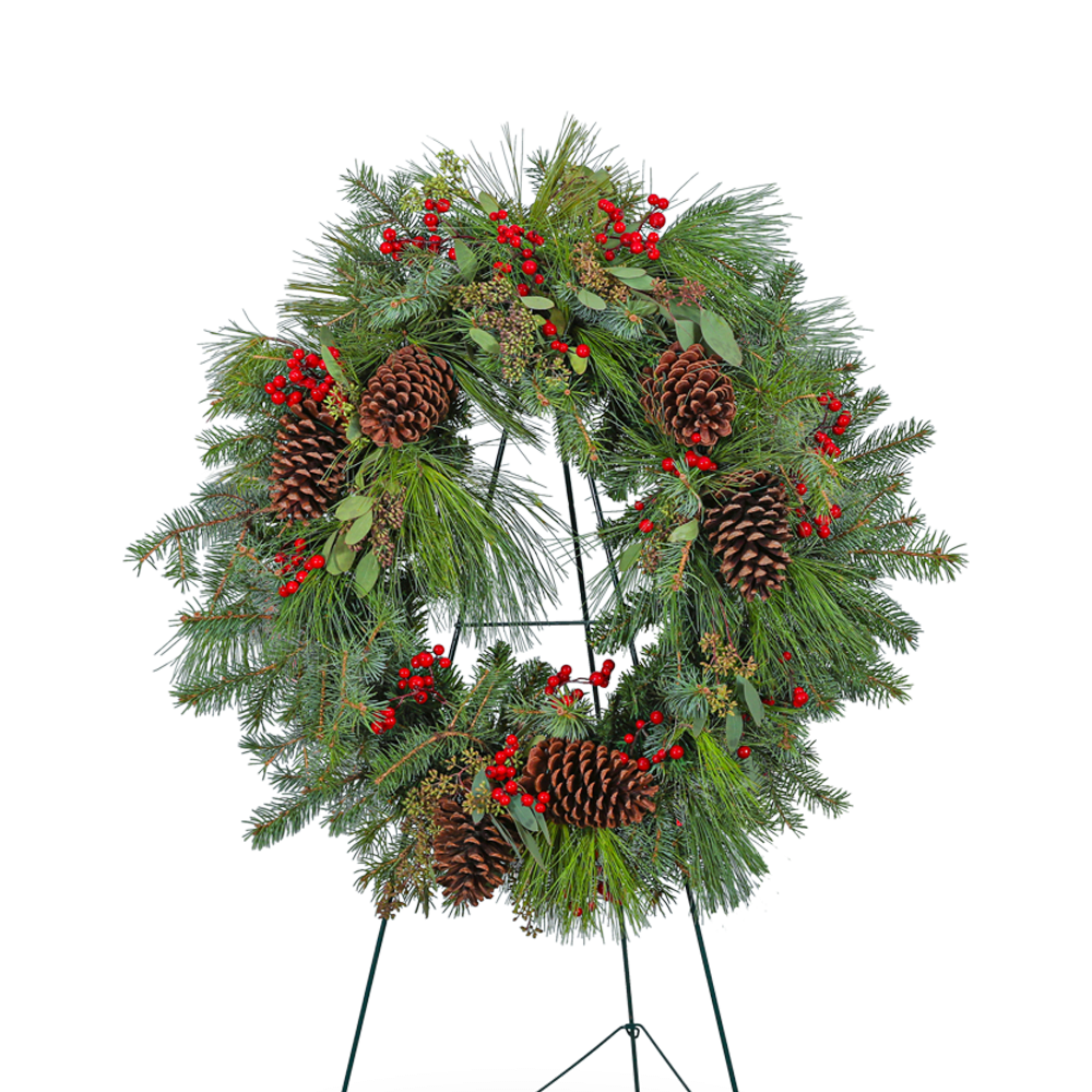 Spirit in the Sky Standing Wreath - Our Spirit in the Sky Standing Wreath is a captivating memorial wreath adorned with eucalyptus, assorted evergreen, pine, red berries, and pinecones. The deep green hues and natural elements evoke a sense of tranquility and connection to the beauty of the forest. This standing wreath serves as a peaceful and timeless tribute, honoring your loved one with the serenity of a woodland sanctuary.