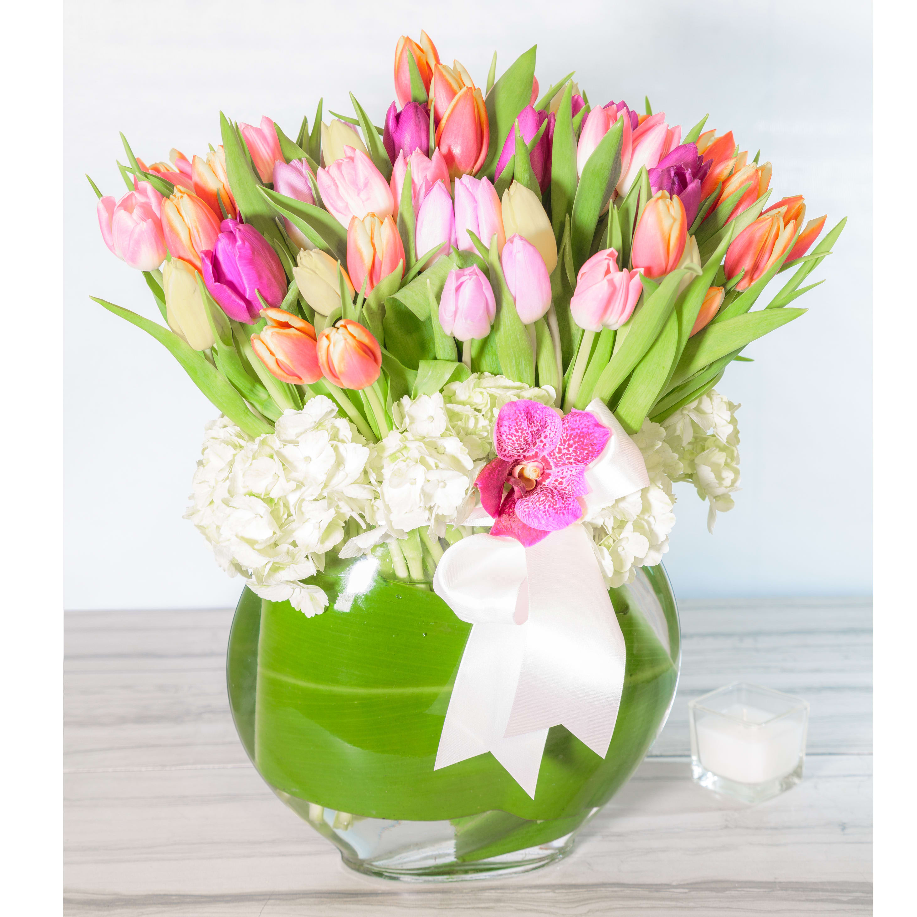 Colors of Joy - This grand and graceful colorful mix of 50 stems of pastel Tulips are embraced by a circle of white lacy Hydrangeas at the base. The leaf-lined glass vase and ribbon put the elegant finishing touches on this impressive design. Stands approximately 30&quot; tall.  Deluxe: 100 stems of Vibrant Tulips in a glass vase Premium: 200 stems of Vibrant Tulips in a glass vase 