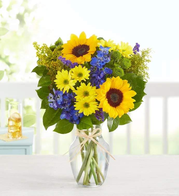 Sunny Fields  - Arrangement filled with yellow daises, sunflowers, blue delphinium, green buttons, and solidago. 