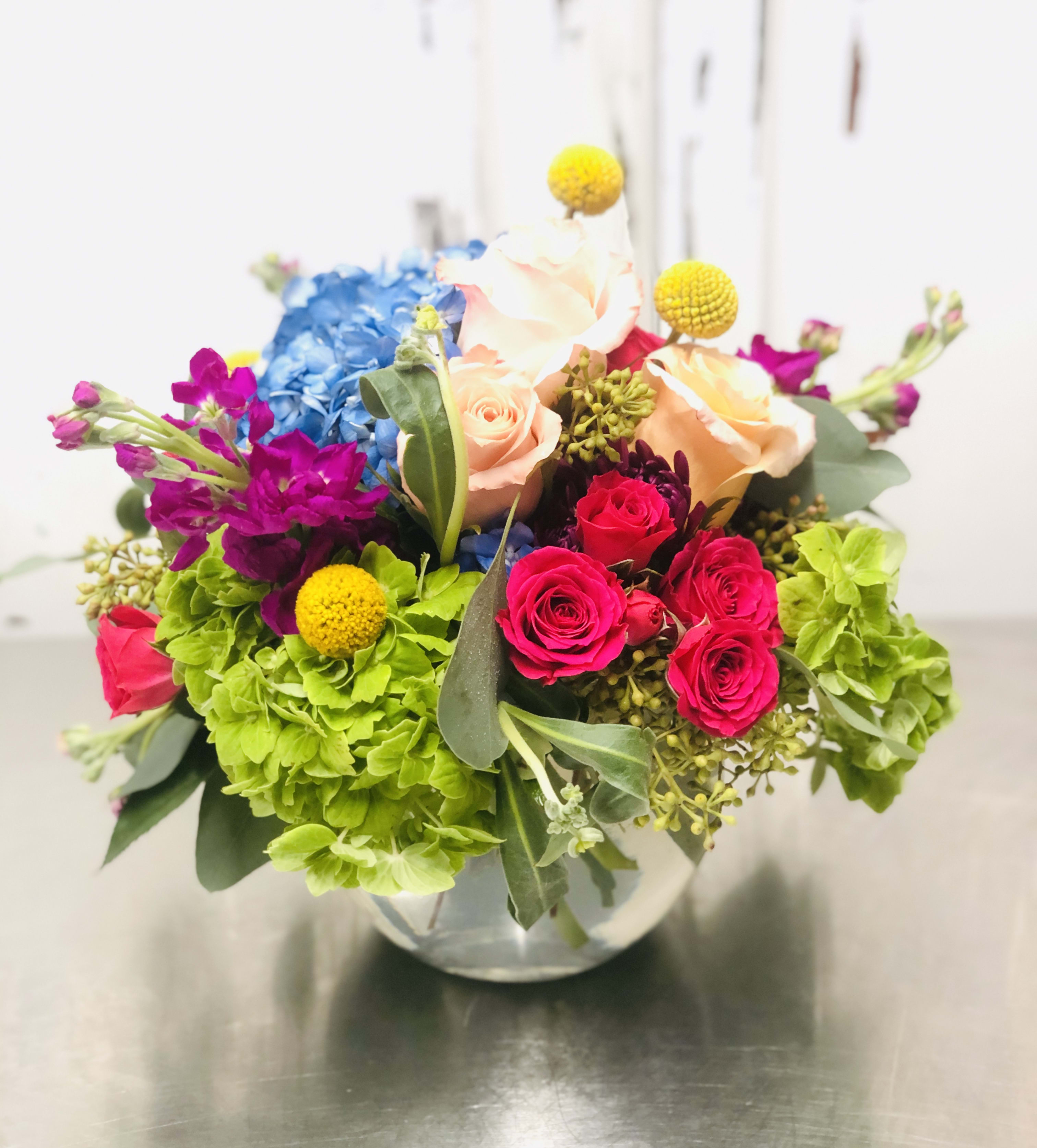 Simply Delightful - This glass globe full of fresh, Spring blooming flowers bursting with color should bring sheer delight to its recipients face.  The assorted variety of flowers in this design will vary depending on season and availability. Hydrangeas, Roses, and assorted flower fillers in bright colors are sure to delight it's recipient. Florist reserves the right to make modifications to the design based on seasonality and accessibility of blooms and vases.  Any modifications made will honor the intent, and feeling of the pictured design.  Kindly contact us directly with any specifications or concerns. 