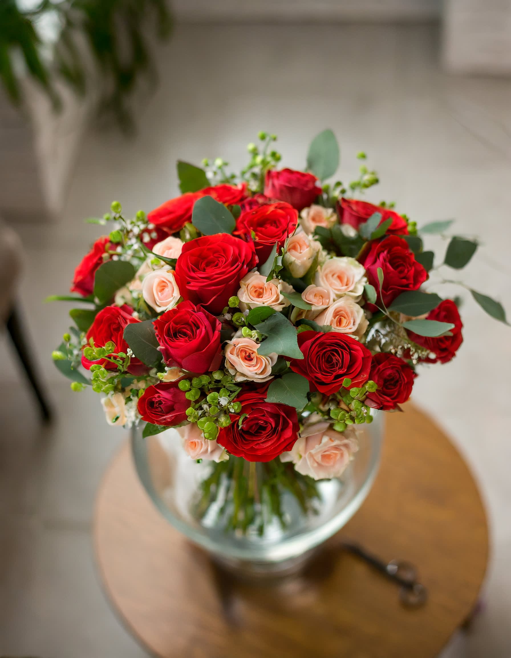 Passion's Flame - A charming and beautiful bouquet featuring red roses and cream spray roses, elegantly arranged in a clear vase. The delightful aroma of eucalyptus adds a fragrant touch to this lovely arrangement.  Disclaimer: ALL IMAGES PROVIDED AT DELUXE PRICE Photos and visual presentation of the products represent an overall style, look and feel, which we may not be able to identically replicate in some instances