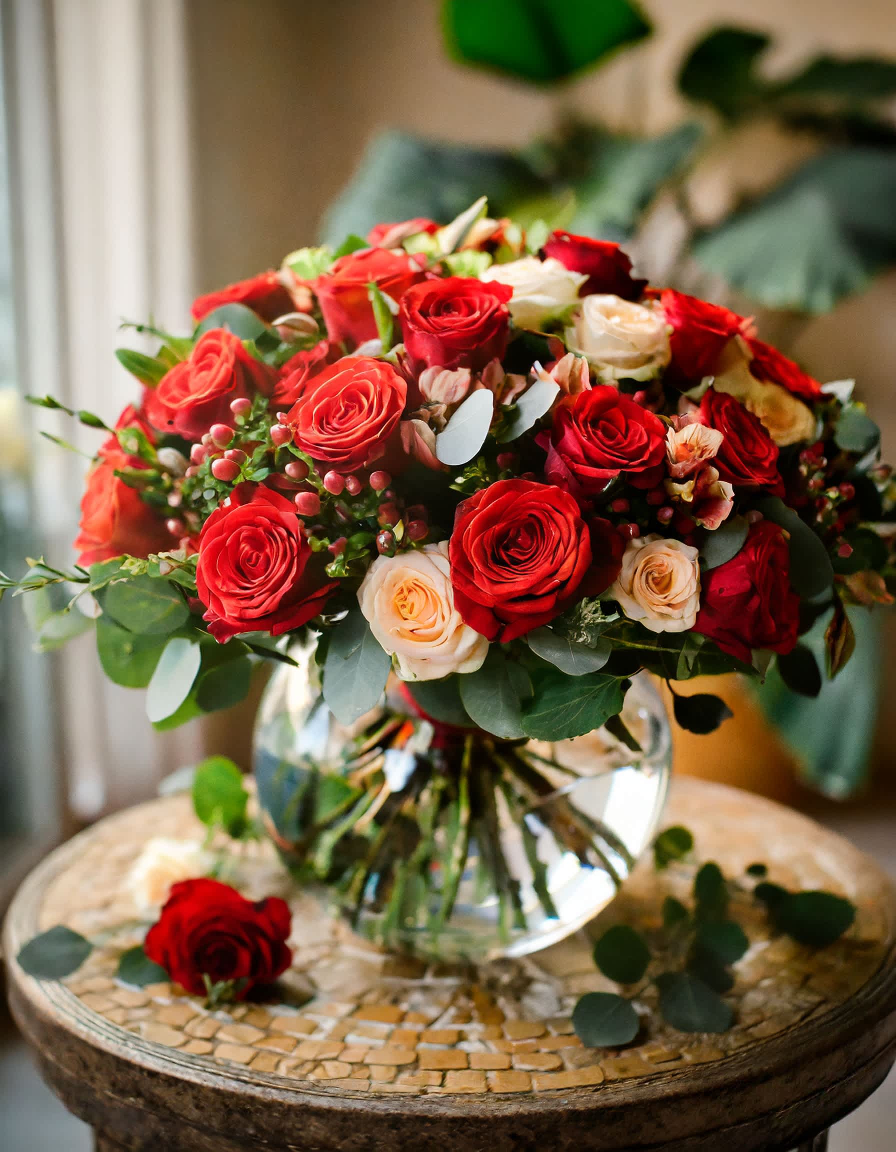 Love Beyond Measure - A charming and beautiful bouquet featuring red roses and cream spray roses, elegantly arranged in a clear vase. The delightful aroma of eucalyptus adds a fragrant touch to this lovely arrangement.  Disclaimer: ALL IMAGES PROVIDED AT DELUXE PRICE Photos and visual presentation of the products represent an overall style, look and feel, which we may not be able to identically replicate in some instances