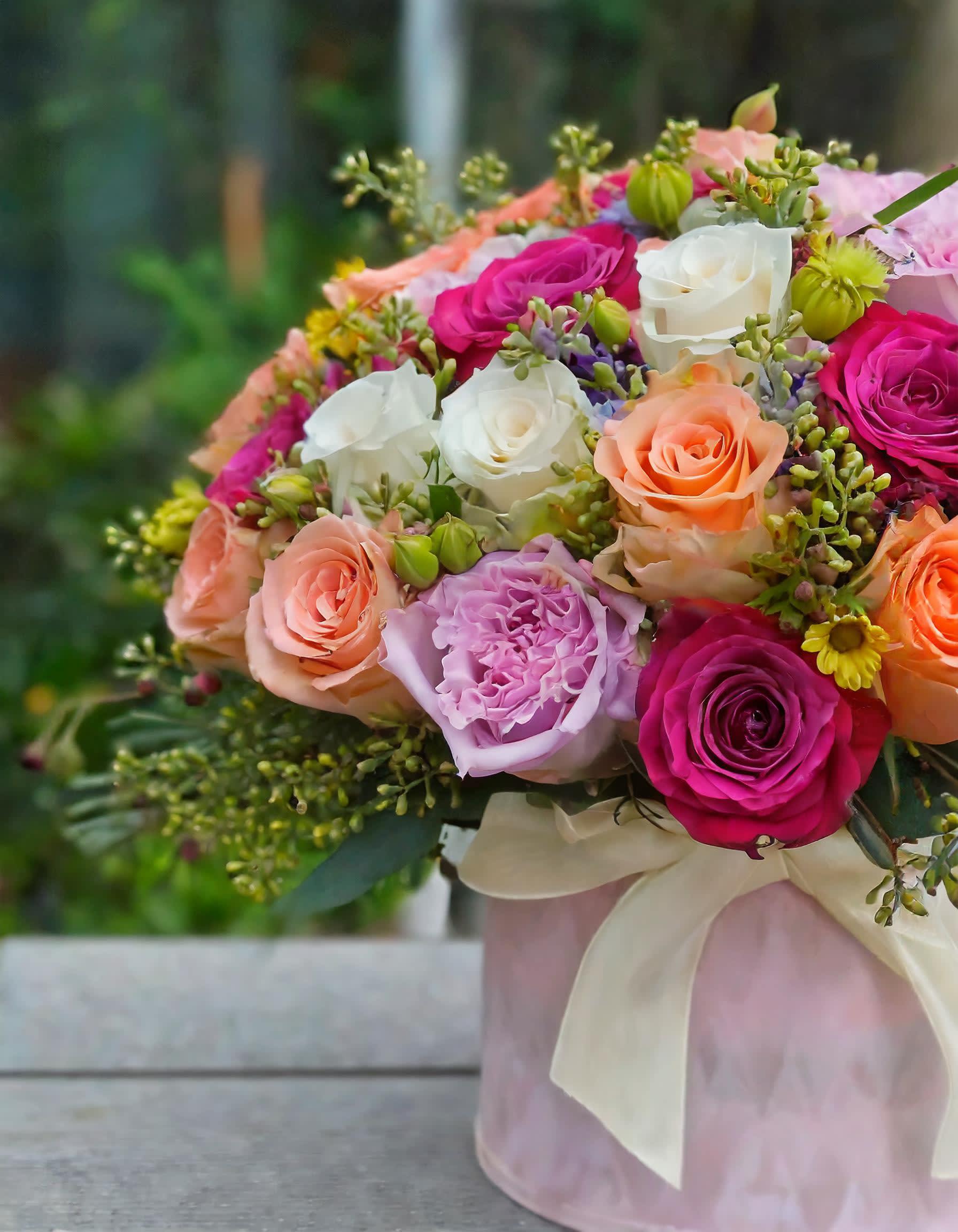 Blossom Banter - Experience romance with our stunning mix of fresh flowers, including pink and peach roses, elegantly arranged in a charming hatbox. Let love blossom with our enchanting floral display.  