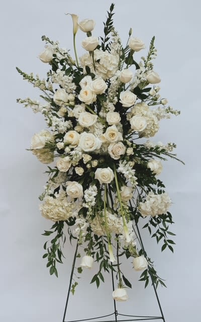 Eternal Peace White Standing Spray By Venetian Flowers  - This elegant sympathy standing spray, designed by Venetian Flowers, embodies grace and serenity, offering a heartfelt tribute during difficult times. The arrangement features a stunning array of pure white blooms, creating a soothing and peaceful visual that conveys compassion and love.  At the base, plush white hydrangeas provide a soft, full foundation, symbolizing heartfelt emotions. Beautiful white roses and delicate garden roses add layers of elegance, their classic beauty representing love and remembrance. The inclusion of white lisianthus introduces a touch of refined charm, while delicate stock flowers enhance the texture and fill the arrangement with a gentle fragrance.  Interspersed among these blooms are other seasonal white flowers, carefully chosen to complement the overall design and add depth. The standing spray is gracefully arranged to convey a sense of tranquility and support, making it a fitting tribute for honoring a loved one.  Shown In Standard - As pictured Deluxe &amp; Premium will make this spray extra large with more premium flowers added to value. 