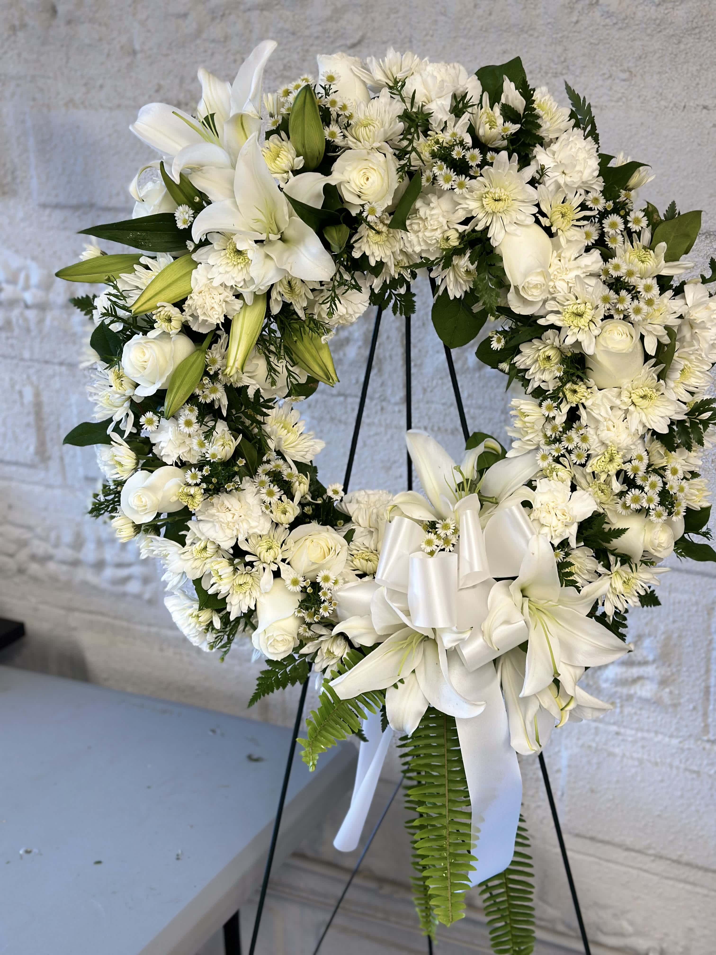 Circle of Serenity Floral Tribute Circle of Serenity Floral Tribute - A radiant standing spray that honors the enduring legacy of your loved one. Adorned with delicate roses, chrysanthemums, and daisies in soft hues, and accentuated with lush green plants, this open circle arrangement symbolizes the unending cycle of love and remembrance. With each bloom representing cherished memories and moments shared, it serves as a comforting reminder of the everlasting bond you hold dear.