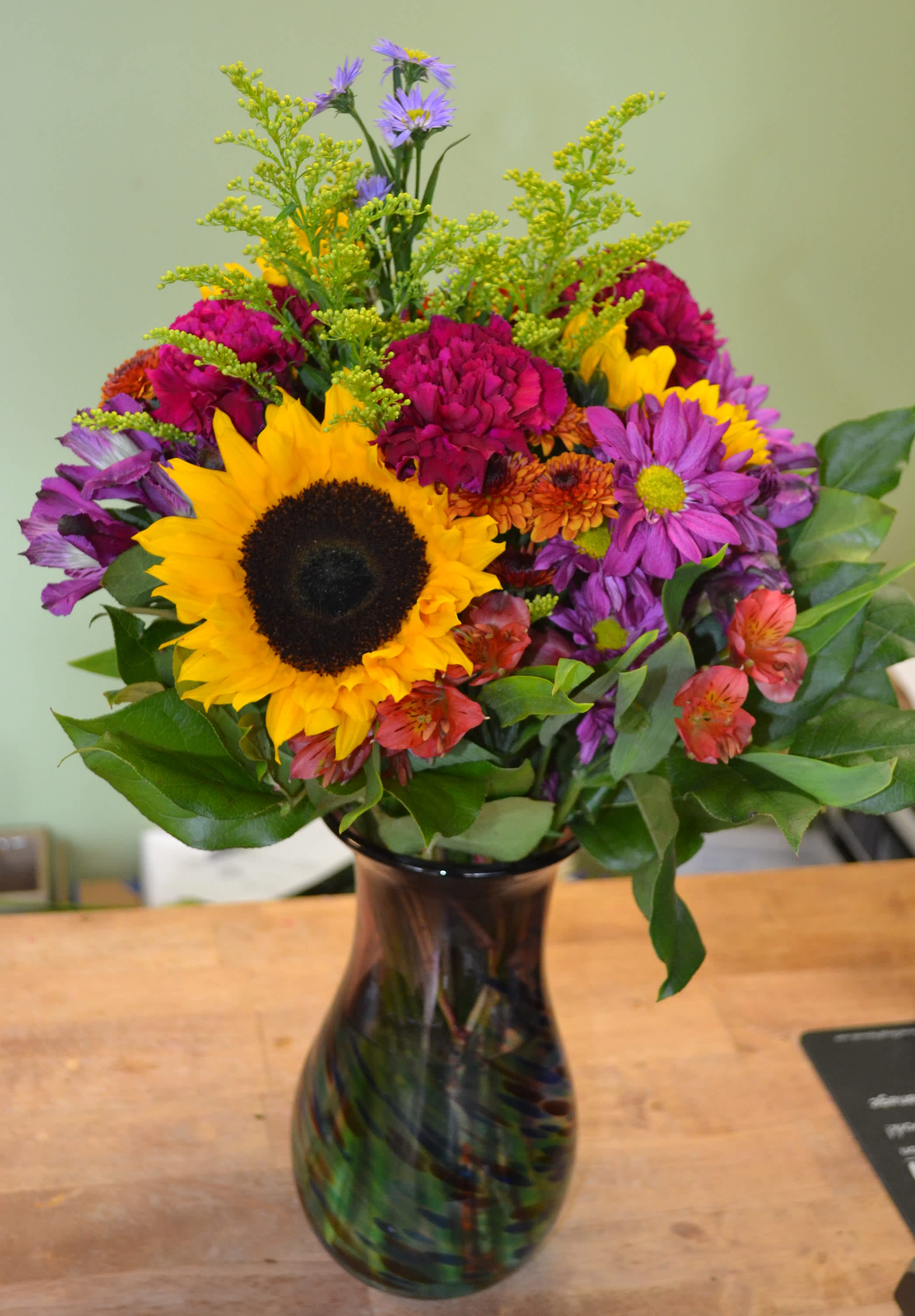 Harvest Sunset - A Brilliant combination of a swirl vase with sunflowers, daisies, carnations, button poms, solidago and alstro